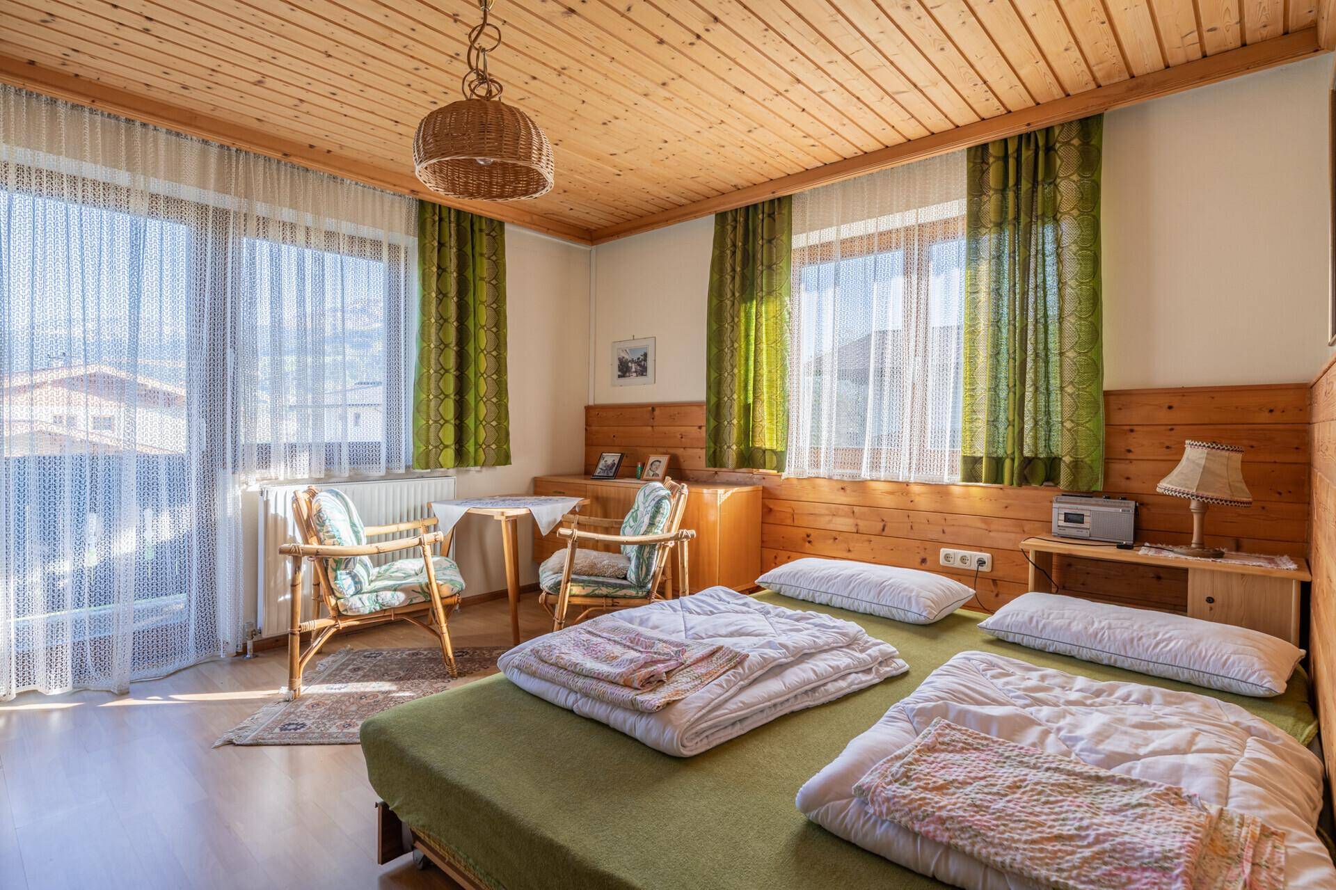 Helles Schlafzimmer mit Holzbalkendecke, Zugang zum Balkon und traditionellen Holzmöbeln.