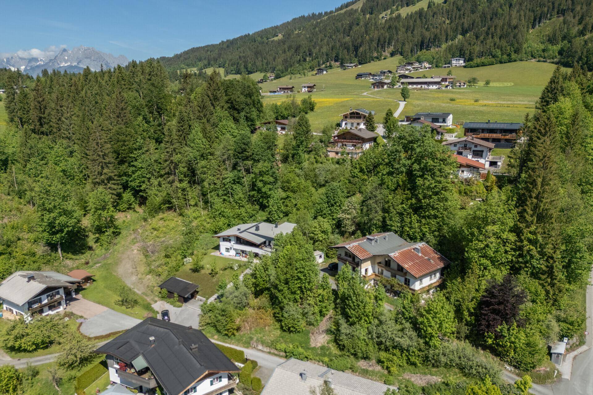 Panoramablick auf eine Wohnsiedlung in einer grünen Berglandschaft mit traditionellen Häusern und üppiger Vegetation.