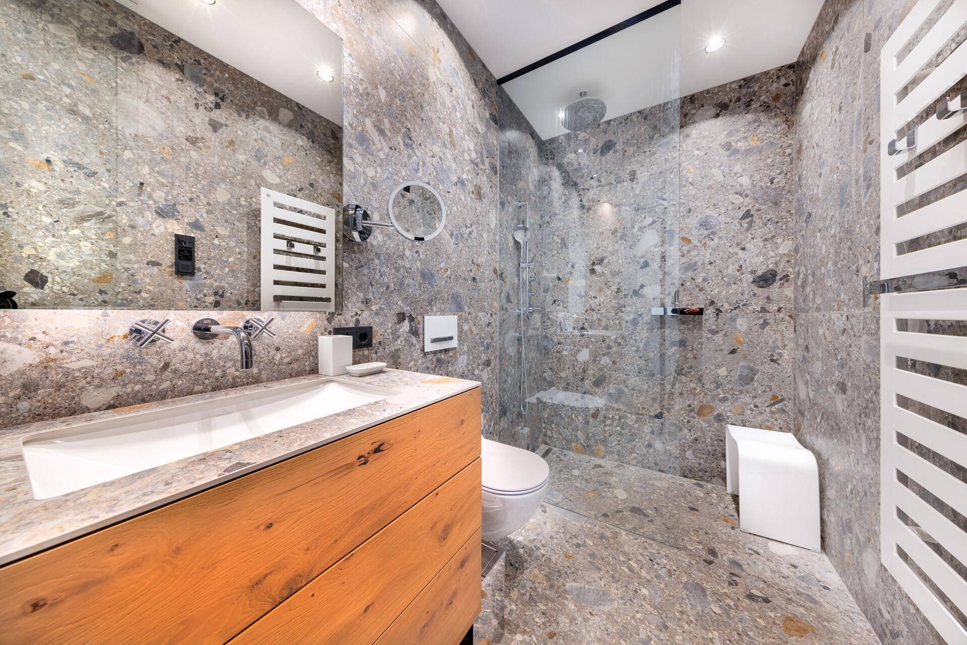 Elegantes Badezimmer mit großformatigen Steinfliesen, begehbarer Dusche und modernem Waschtisch.