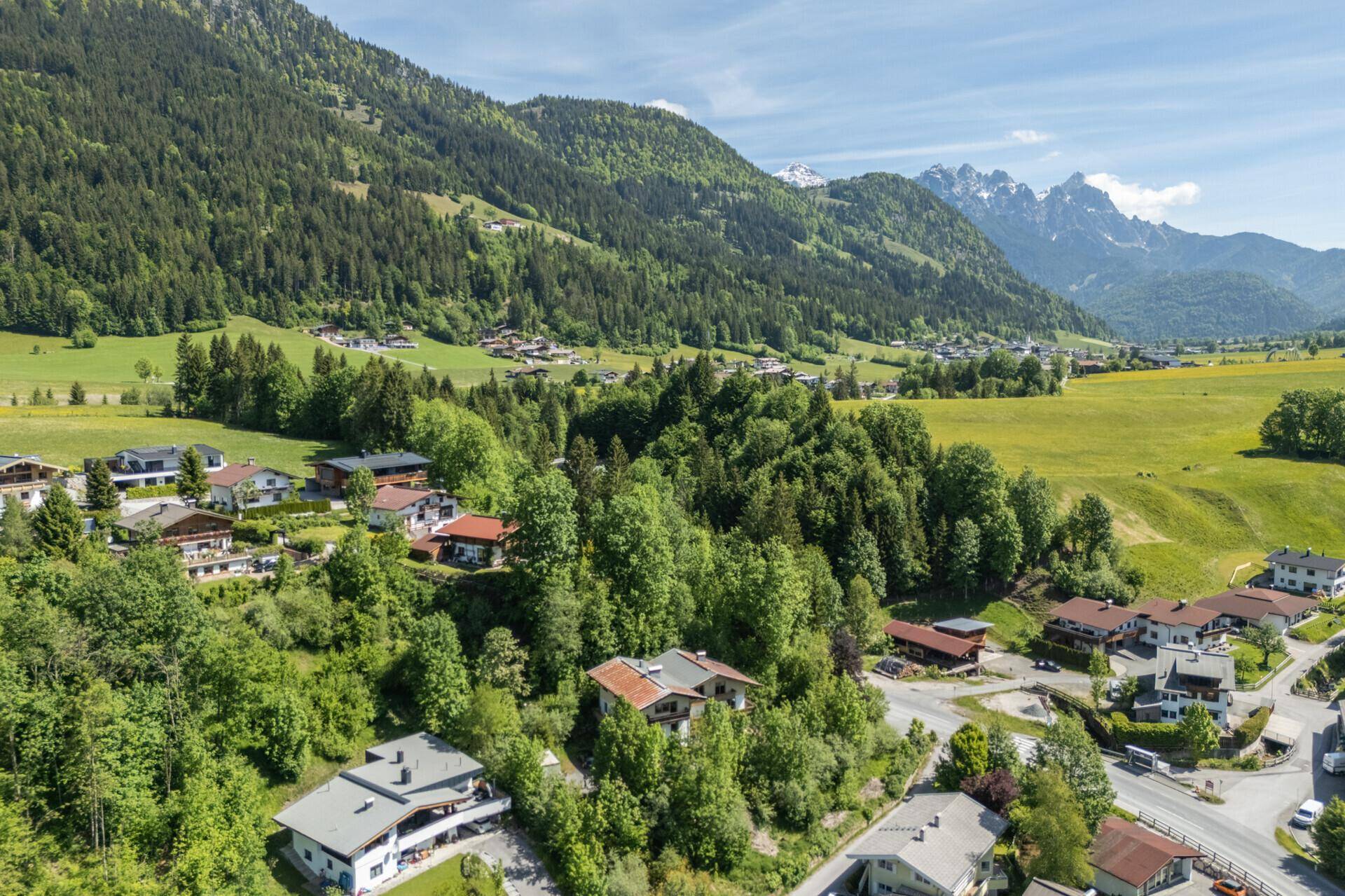 Idyllische Landschaftsaufnahme eines Dorfes in den Alpen, mit weiten Wiesen, Wäldern und beeindruckendem Bergpanorama.
