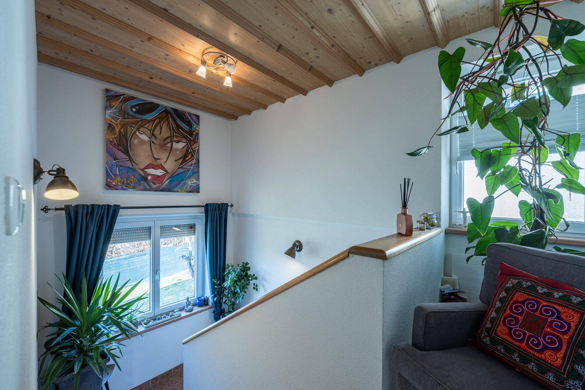 Heller Treppenaufgang mit Holzdecke, großem Fenster und dekorativer Kunst an der Wand.