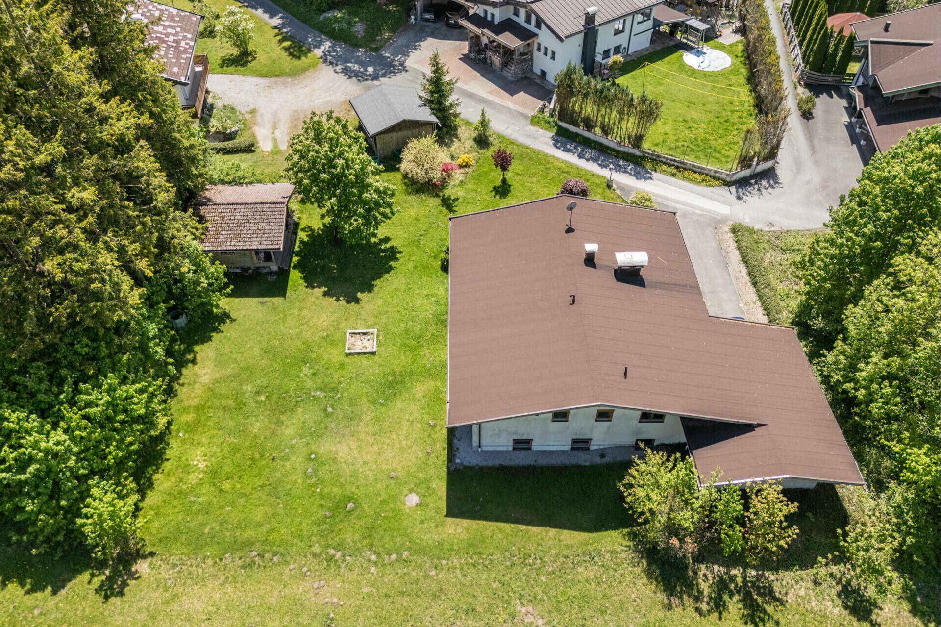 Rückansicht des Hauses mit großem Gartenbereich, umgeben von Bäumen und einem kleinen Schuppen.