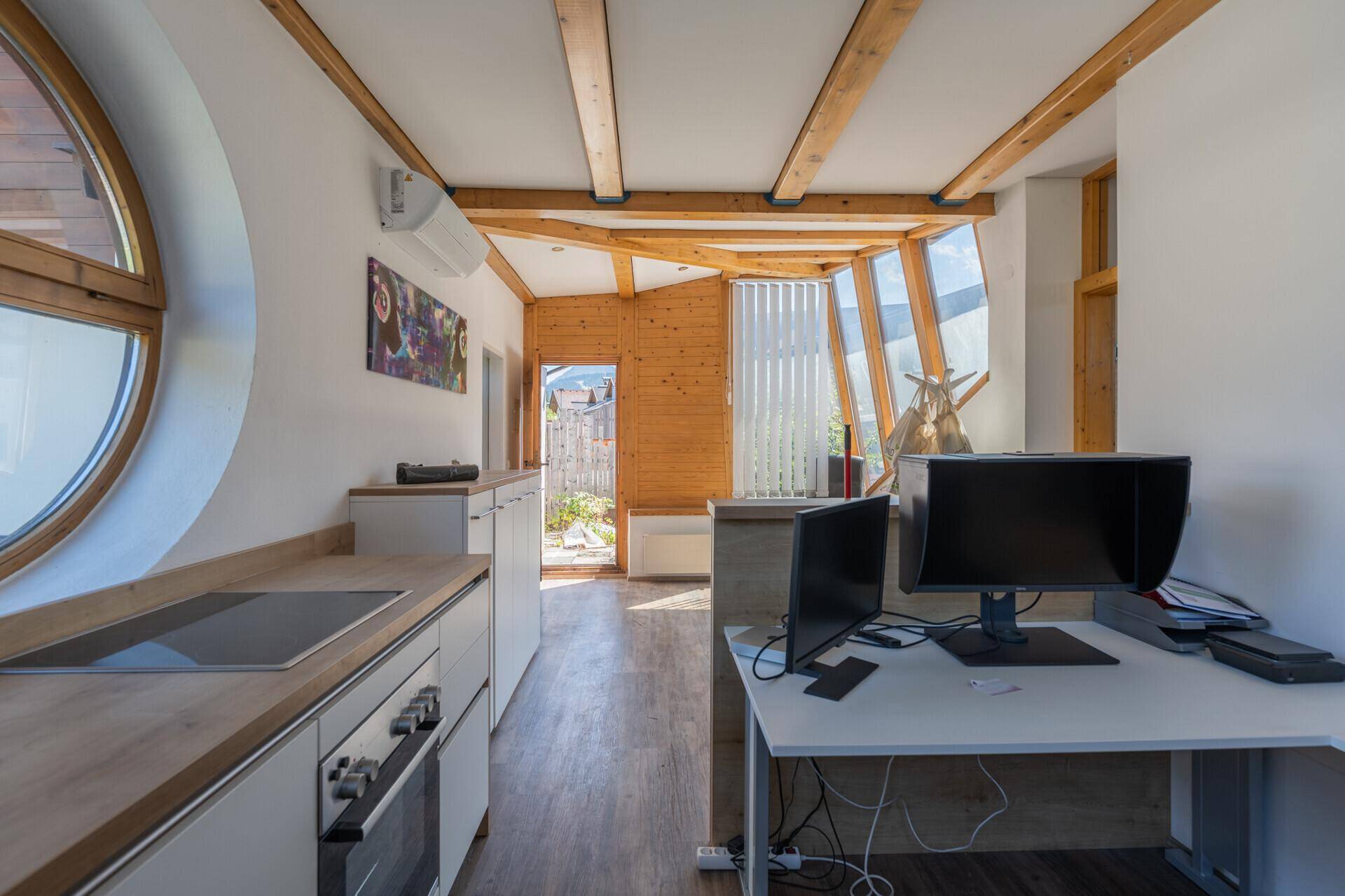 Büro mit Küchenzeile, Holzbalken, großen Fenstern und Zugang zum Außenbereich, hell und funktional.