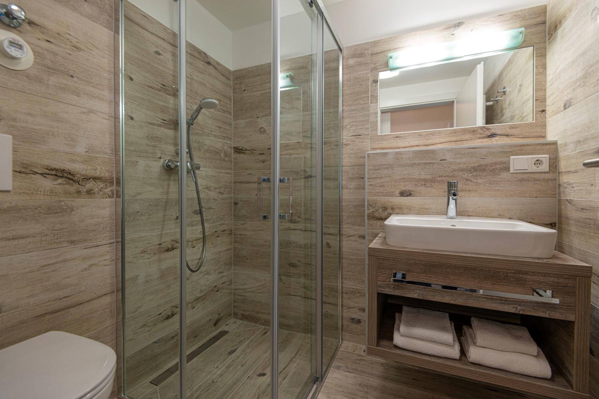 Modernes Badezimmer mit begehbarer Dusche und Holzoptik-Fliesen an Wänden und Boden.