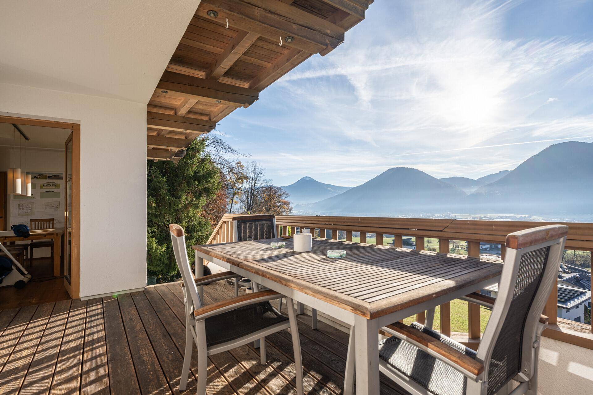 Sonniger Balkon mit Holzboden, Esstisch und atemberaubendem Panoramablick auf die Berge und das Tal.