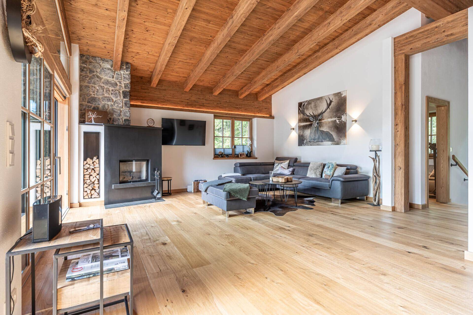 Geräumiges Wohnzimmer mit Kamin, Holzbalkendecke und großen Fenstern.