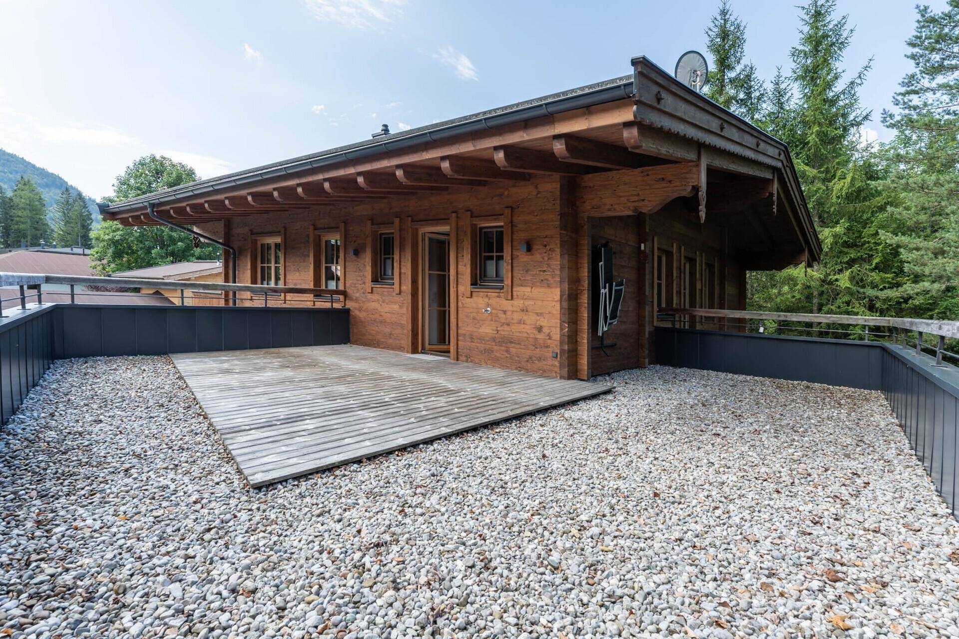 Große Kiesterrasse neben einem Holzhaus mit Blick auf die umliegende Natur.