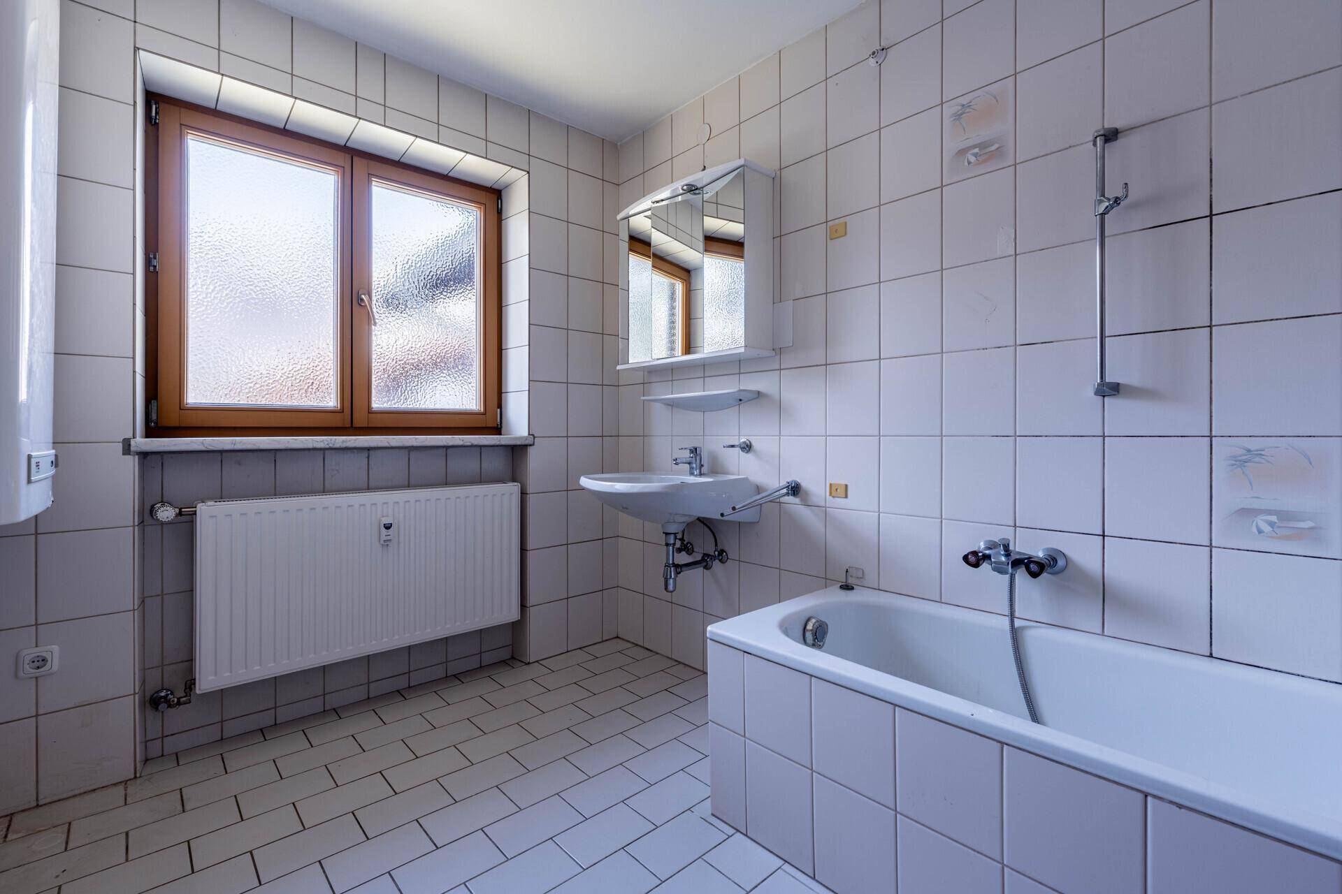 Gefliestes Badezimmer mit Badewanne, Waschbecken und Fenster für ausreichend Tageslicht.