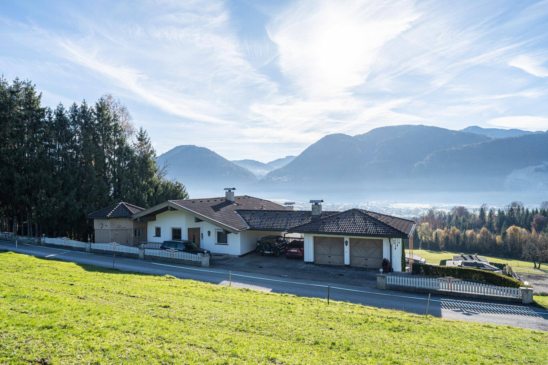 Weitläufiges Anwesen mit Haus und Garagen, eingebettet in eine grüne Hügellandschaft mit Bergblick.