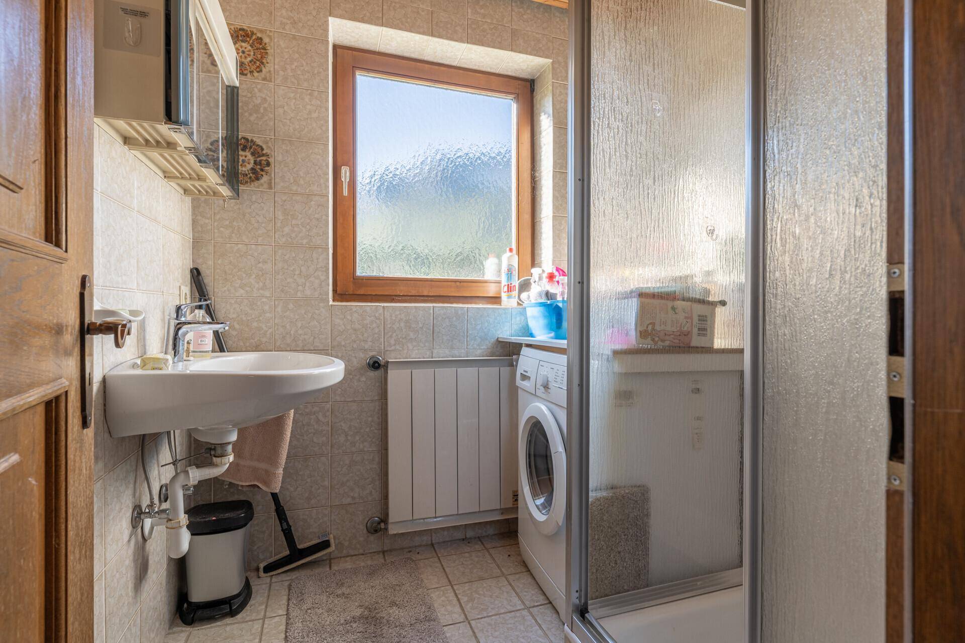 Funktionales Badezimmer mit Dusche, Waschbecken, Fenster und Waschmaschine.