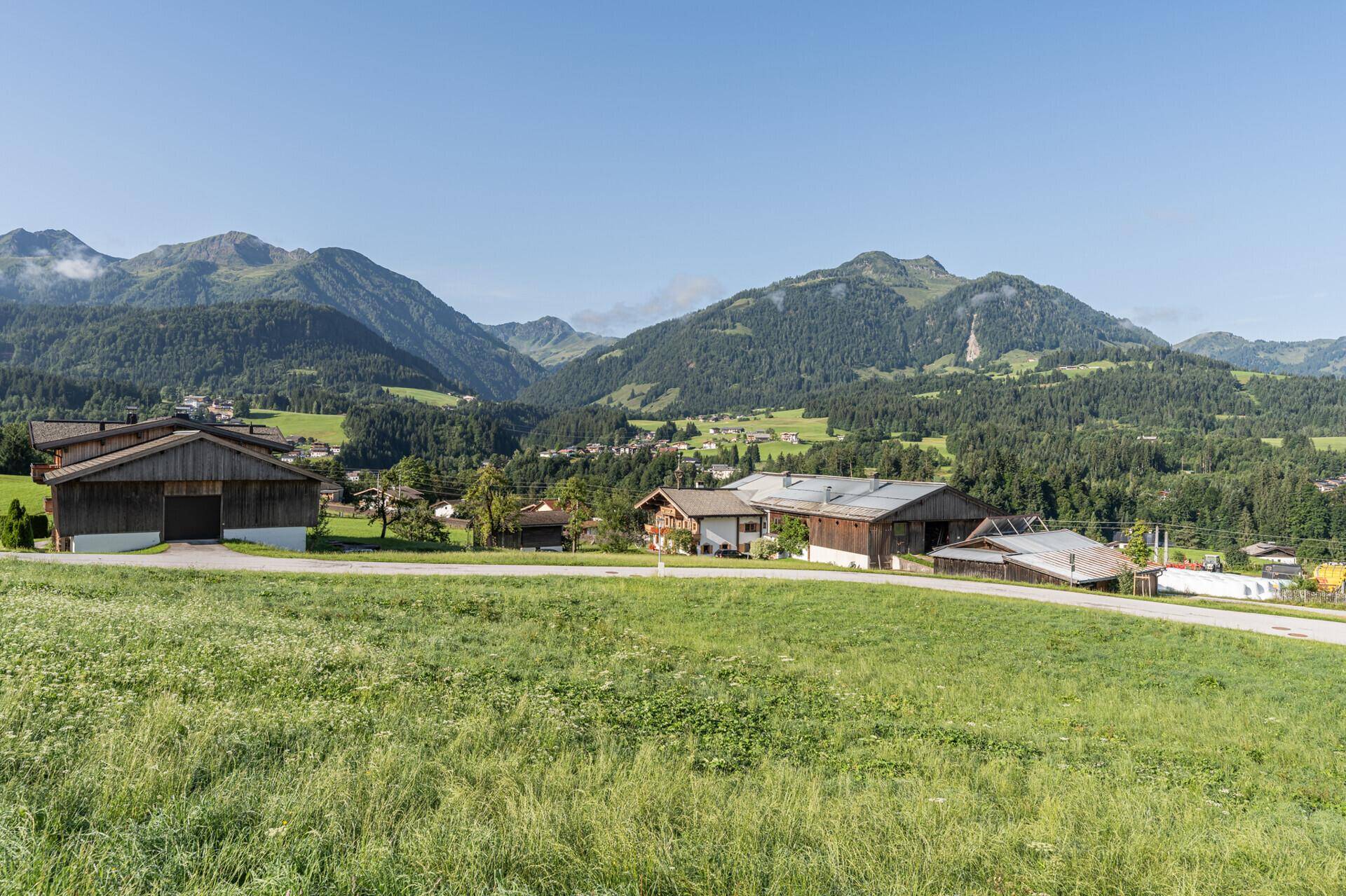 Panoramablick auf eine ländliche Siedlung mit traditionellen Gebäuden und grünen Hügeln unter klarem Himmel.