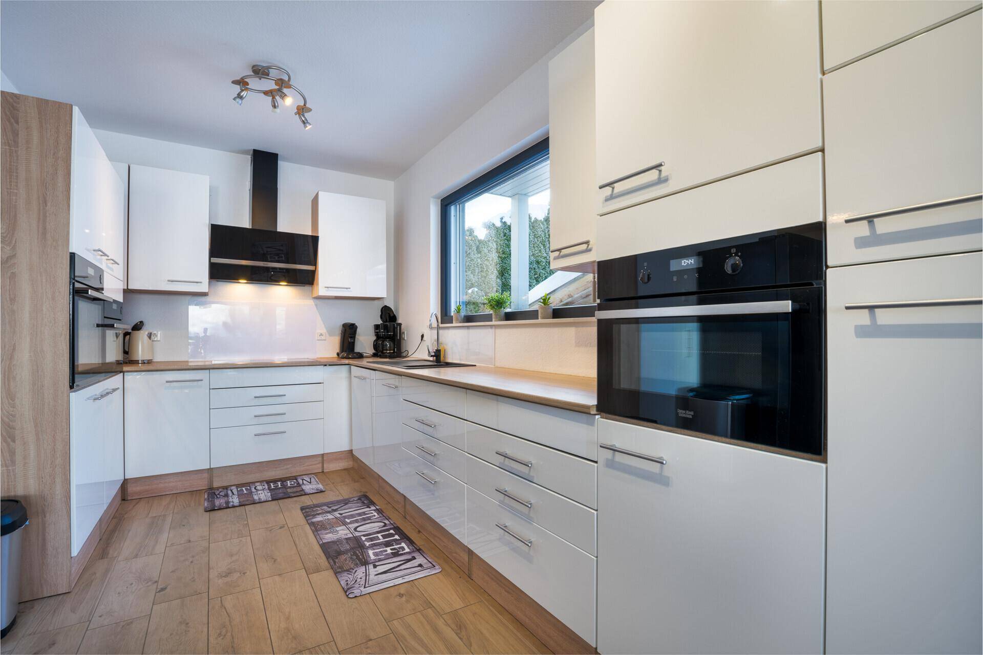 Moderne Küche mit weißen Hochglanzfronten, integrierten Geräten und Fenster.