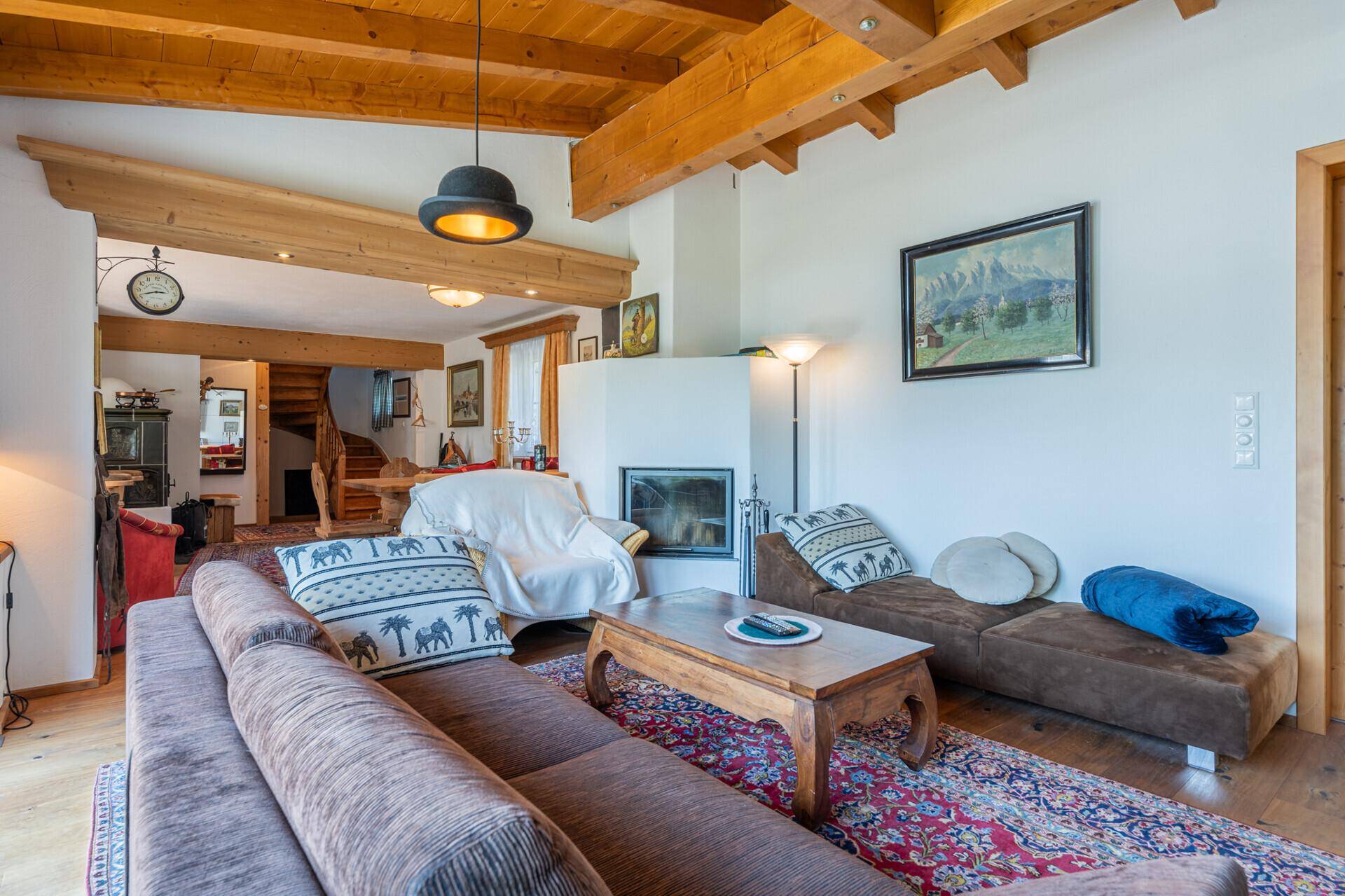 Geräumiges Wohnzimmer im alpinen Stil mit Holzbalken, Kamin und traditionellem Teppich.