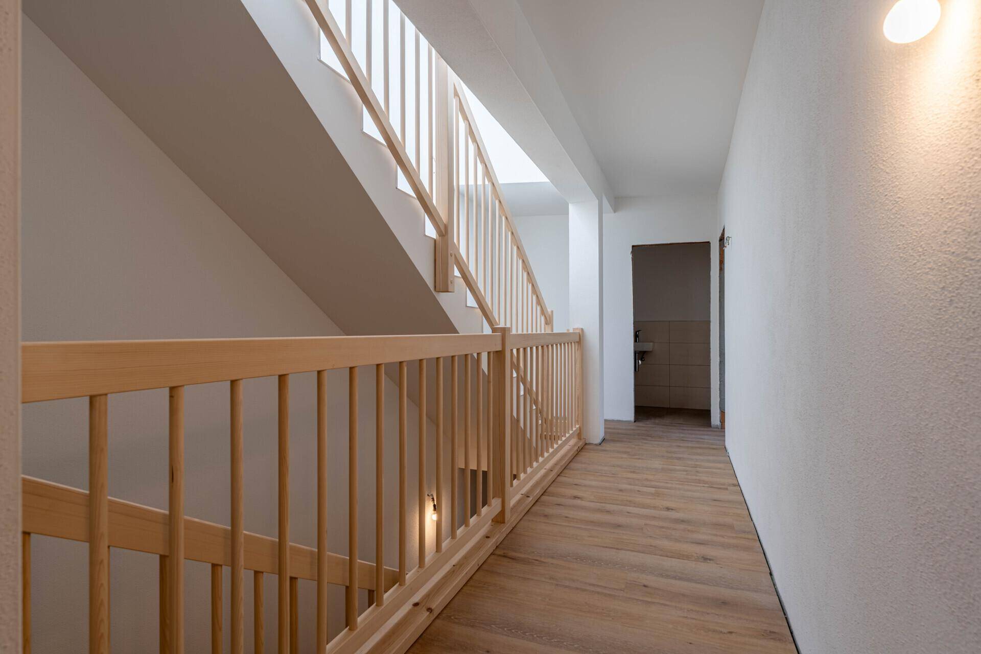 Heller Flur mit Holztreppe und Parkettboden, der zu weiteren Räumen führt.