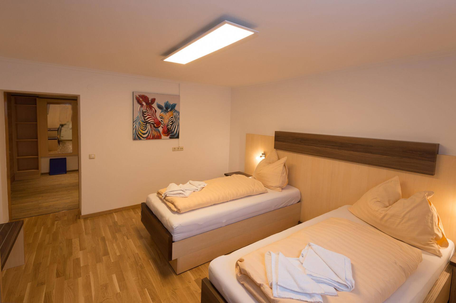 Helles Schlafzimmer mit zwei Einzelbetten, Holzboden und einem farbenfrohen Kunstwerk an der Wand.