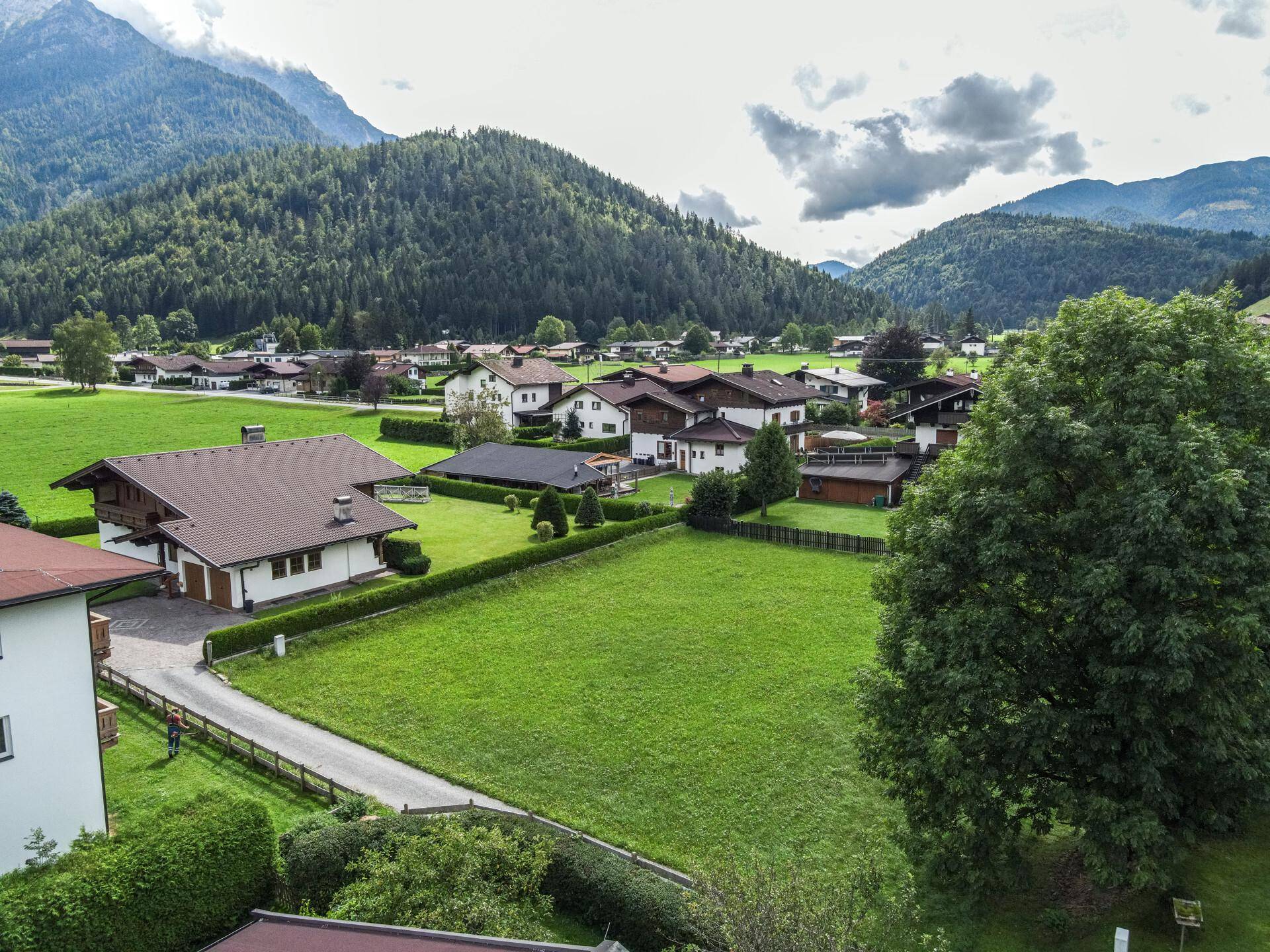 Aussicht auf ein großes, grünes Grundstück mit angrenzender Wohnbebauung und beeindruckender Bergkulisse.