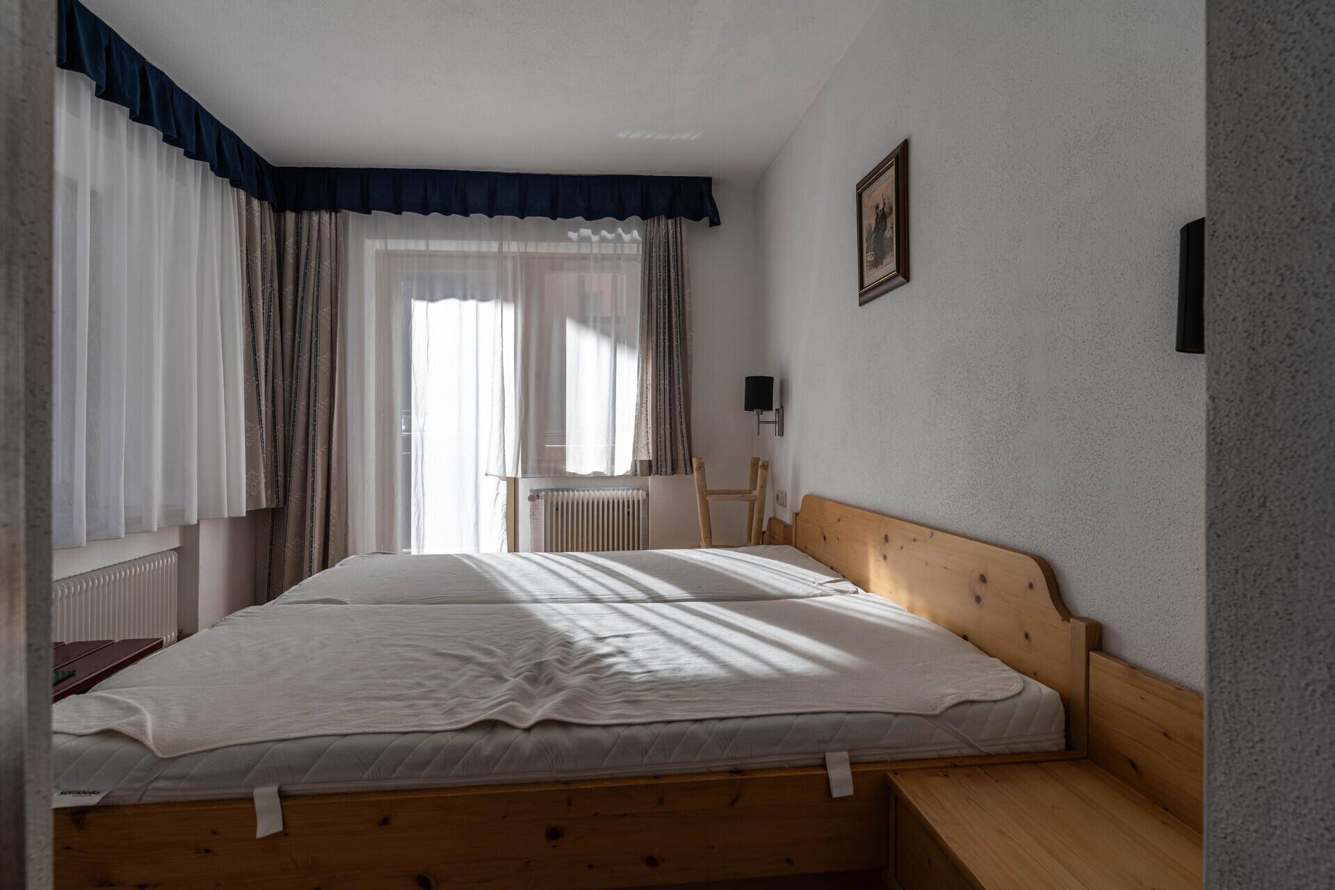 Helles Schlafzimmer mit zwei Einzelbetten, Holzrahmen und Zugang zu einem Balkon.