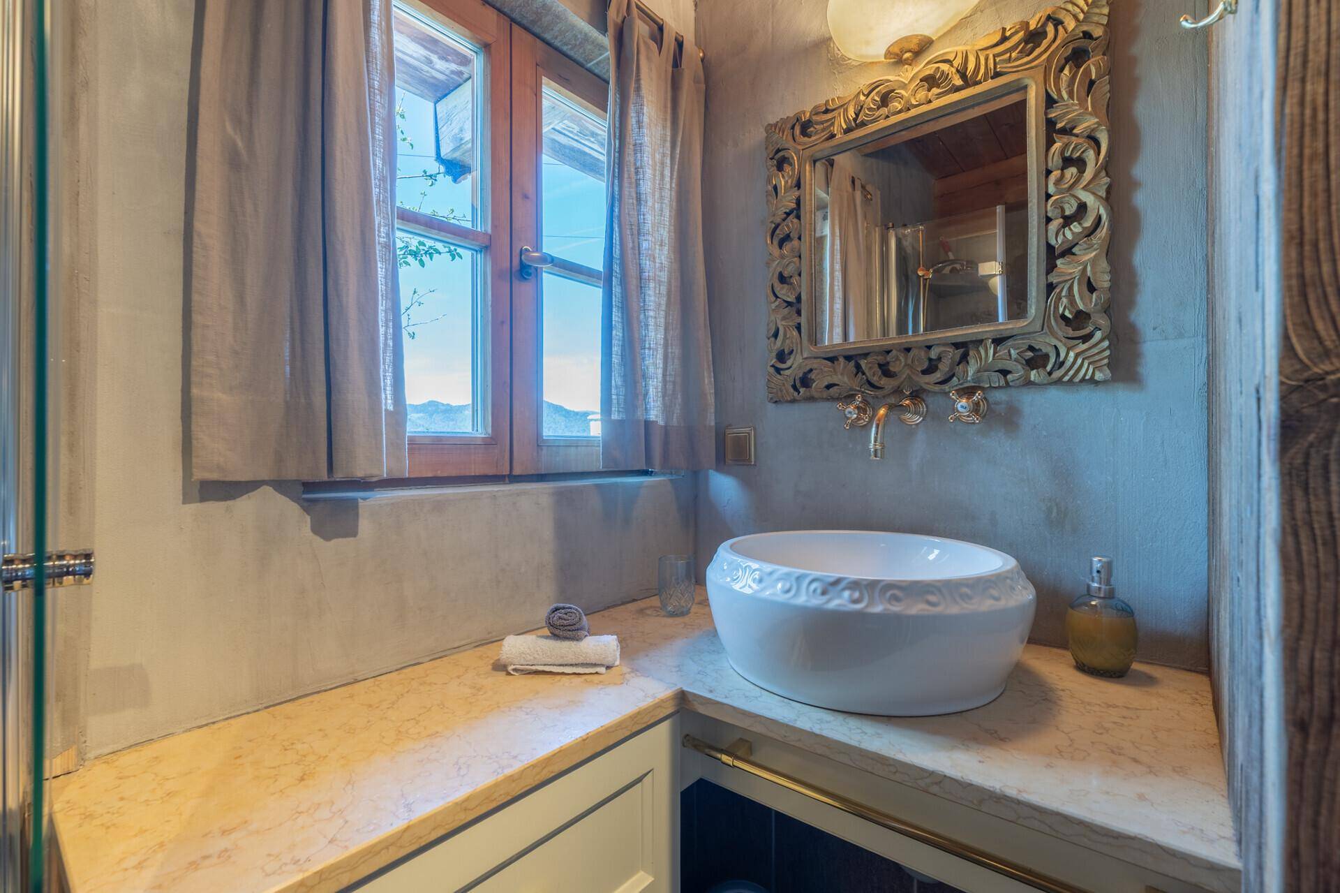 Modernes Badezimmer mit Aufsatzwaschbecken, goldenem Spiegel und Bergblick durch das Fenster.