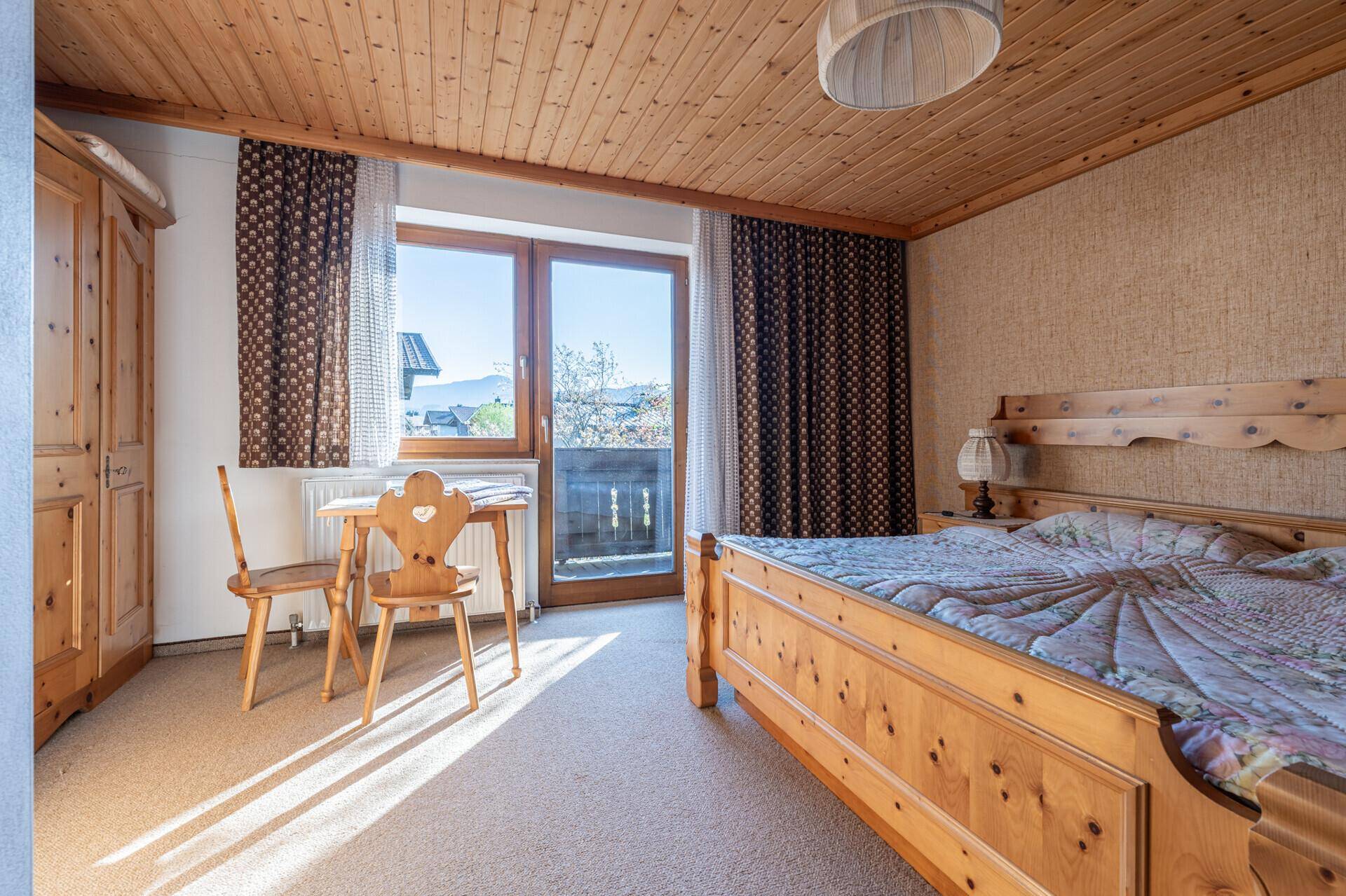 Rustikales Schlafzimmer mit Holzbett, Teppichboden und Zugang zu einem kleinen Balkon.