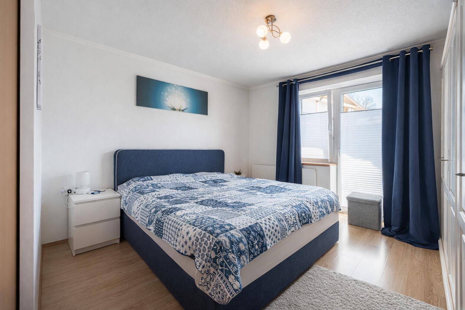 Gemütliches Schlafzimmer mit Doppelbett, Laminatboden und blauen Vorhängen.
