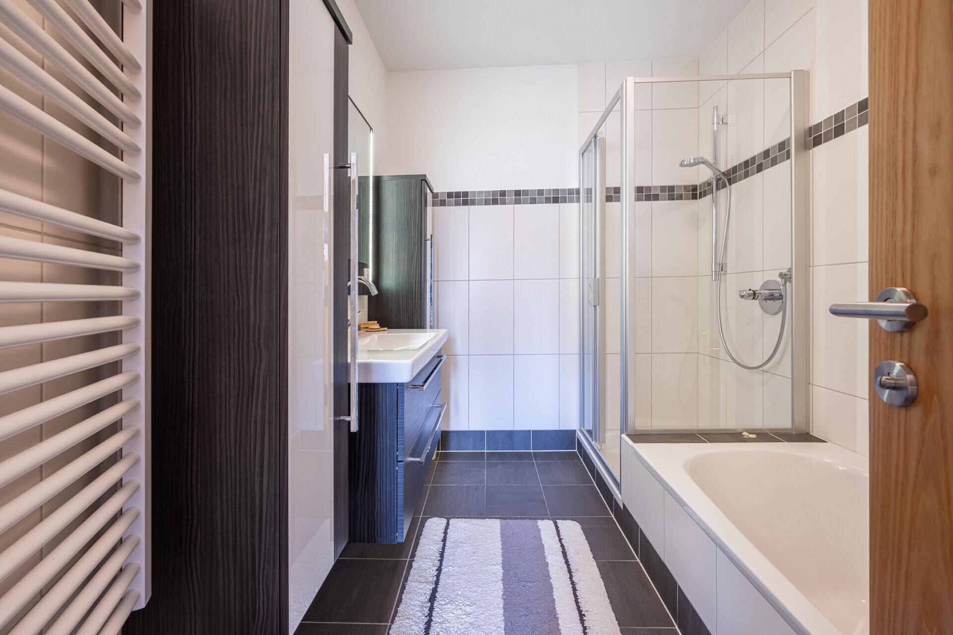 Modernes Badezimmer mit dunklen Bodenfliesen, Dusche, Badewanne und beheiztem Handtuchhalter.