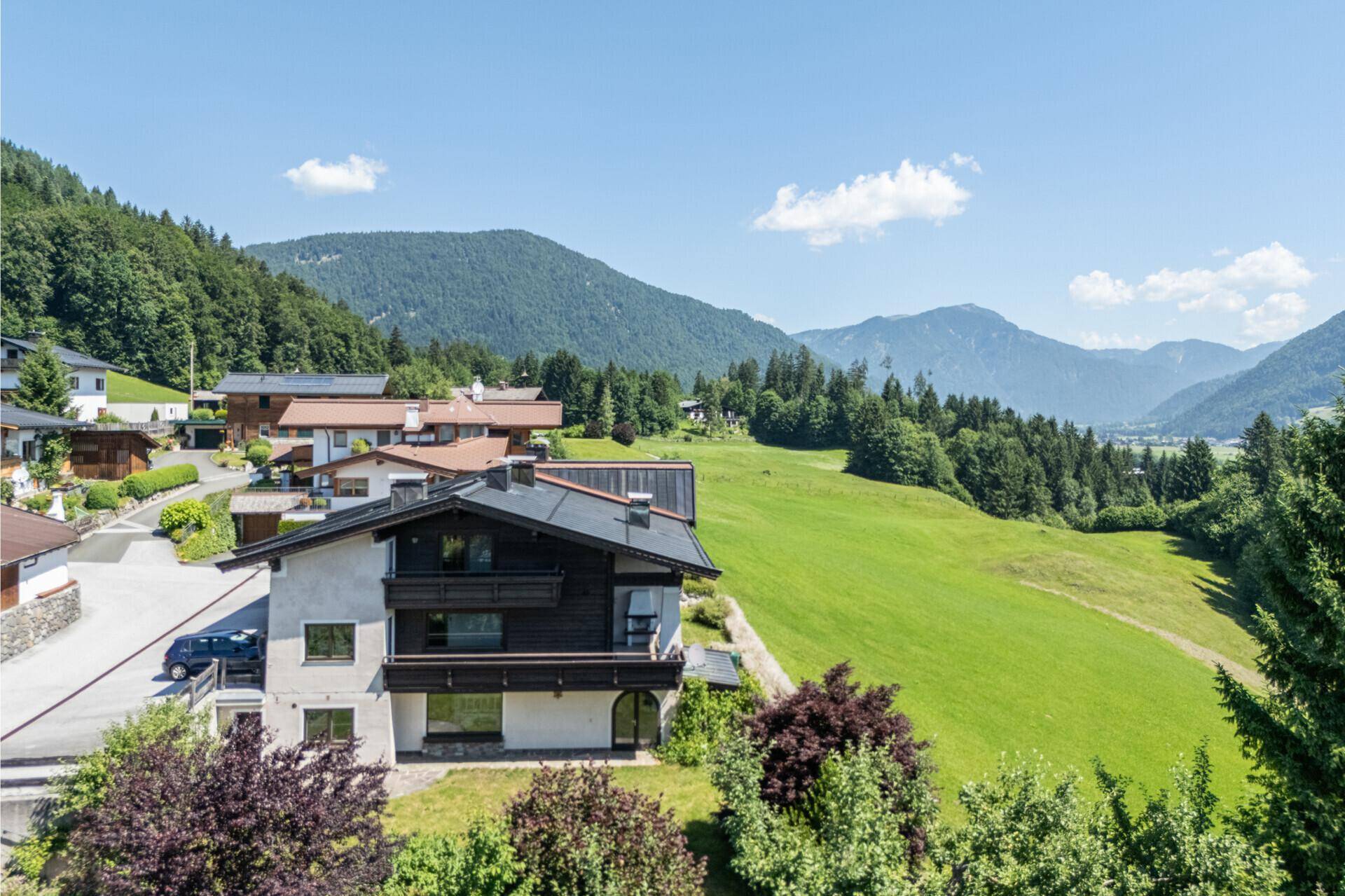 Traditionelles Haus mit Balkonen in einer malerischen Berglandschaft mit grünen Wiesen und Wäldern.