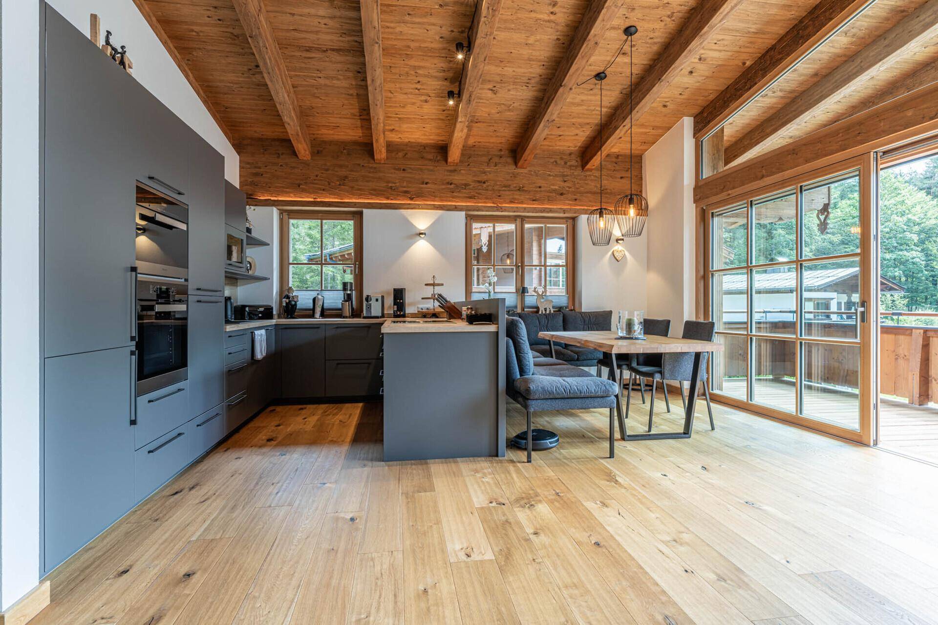 Moderne offene Küche mit Essbereich, Holzbalkendecke und Zugang zur Terrasse.