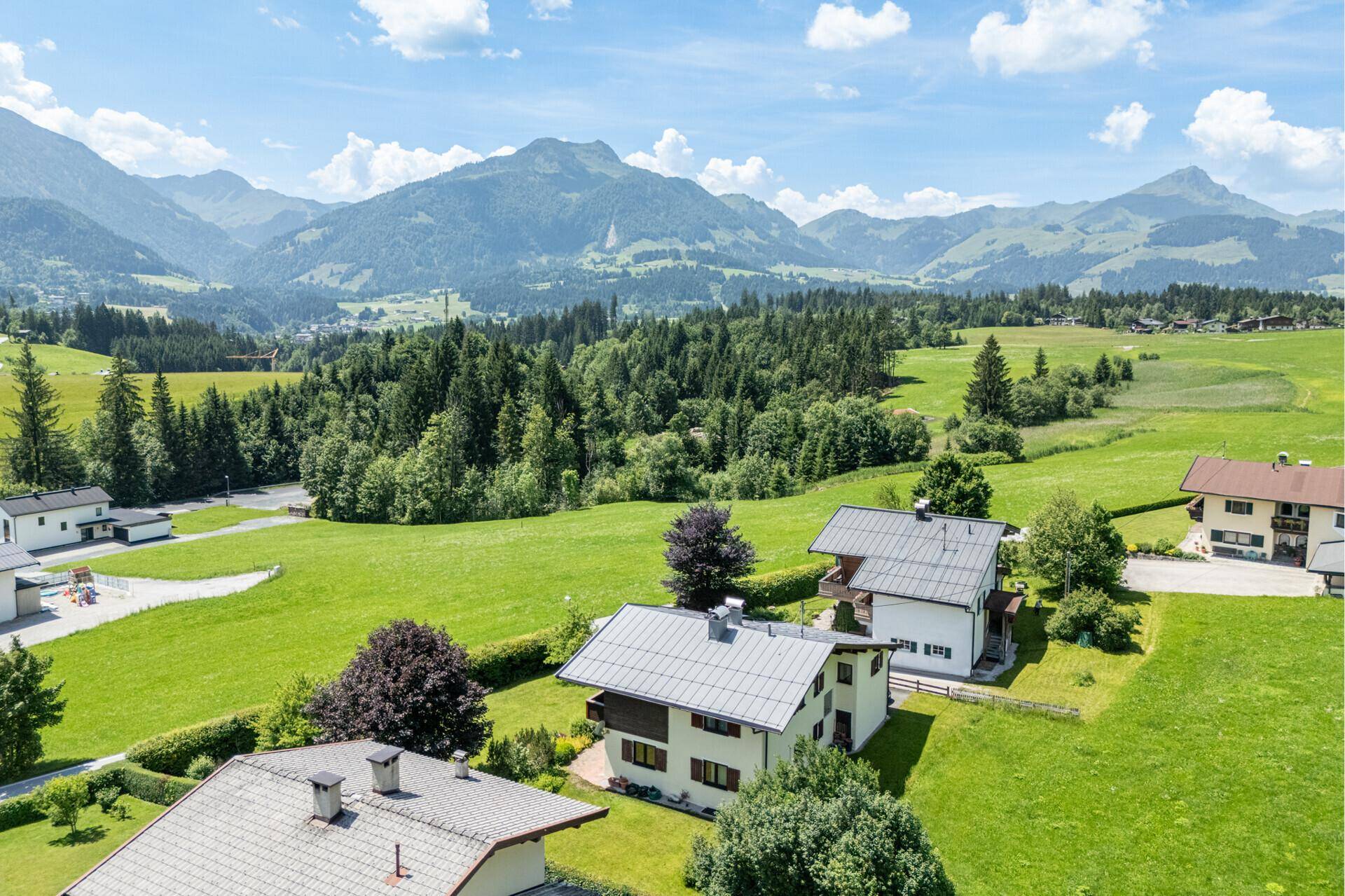 Panoramablick auf eine Wohnsiedlung in einem grünen Tal mit majestätischer Bergkulisse im Hintergrund.