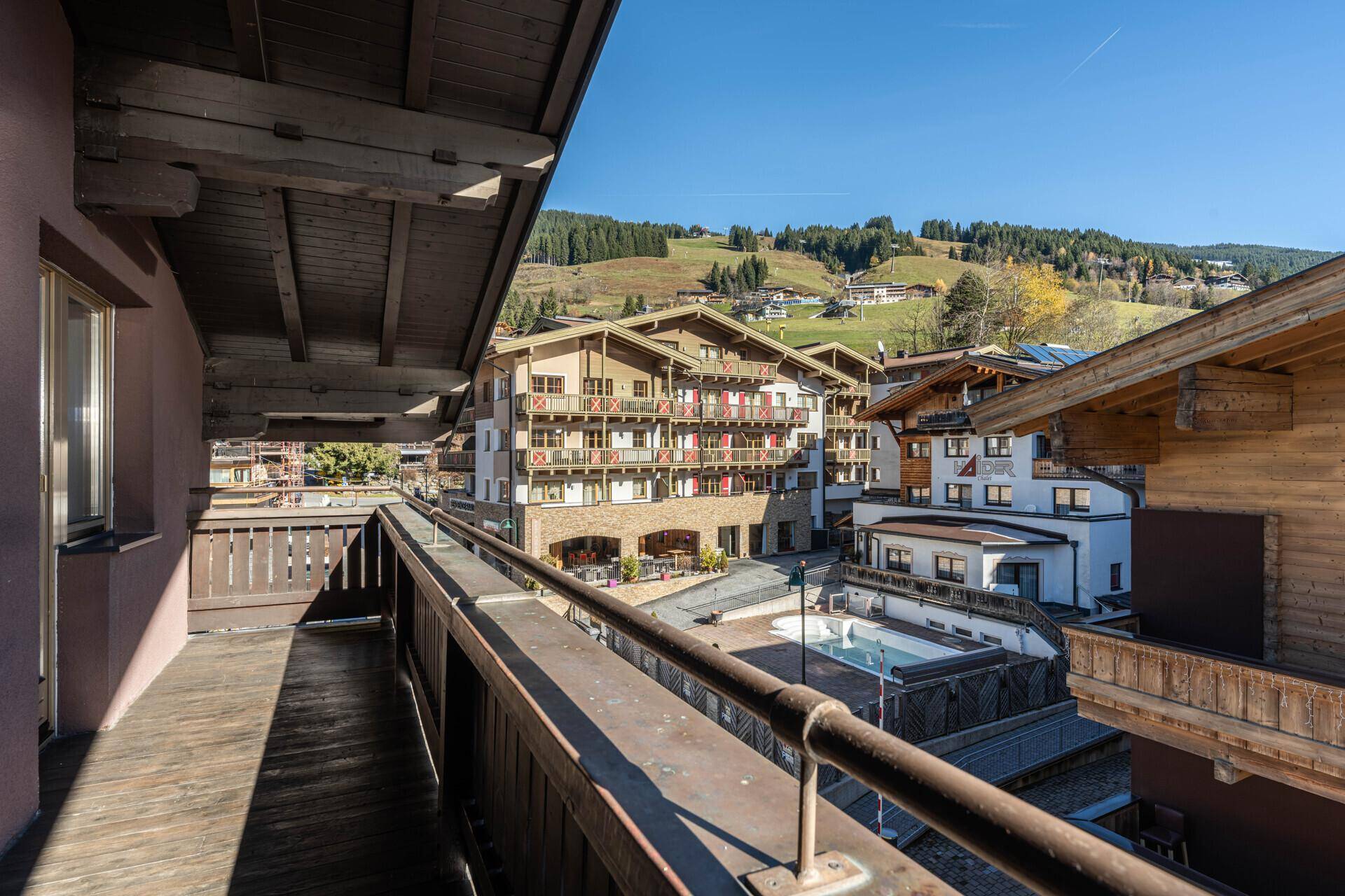 Geräumiger Holzbalkon mit Blick auf umliegende Gebäude und die grünen Berghänge.