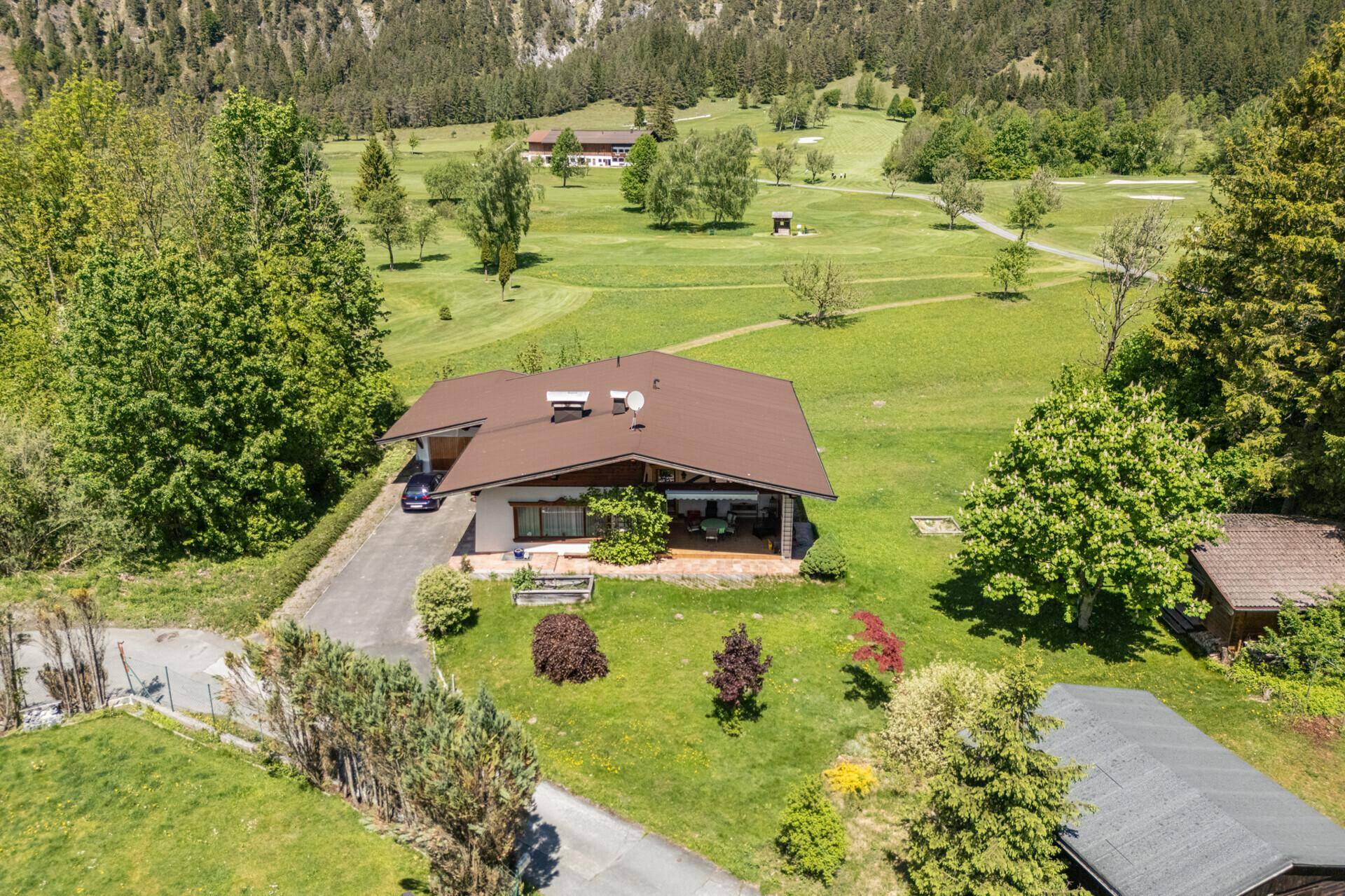 Vorderansicht des Hauses mit Zufahrt, umgeben von gepflegtem Rasen und Bäumen, mit Golfplatz im Hintergrund.