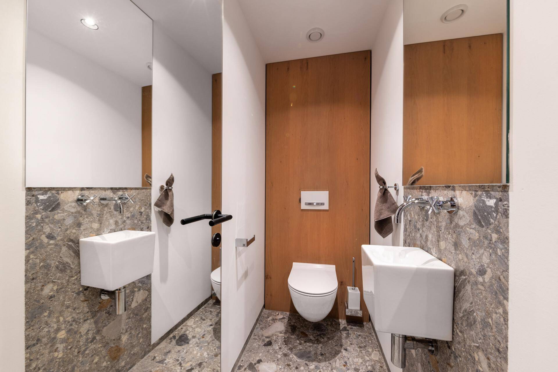 Stilvolles Gäste-WC mit modernen Steinfliesen, Wand-WC und kleinem Waschbecken.