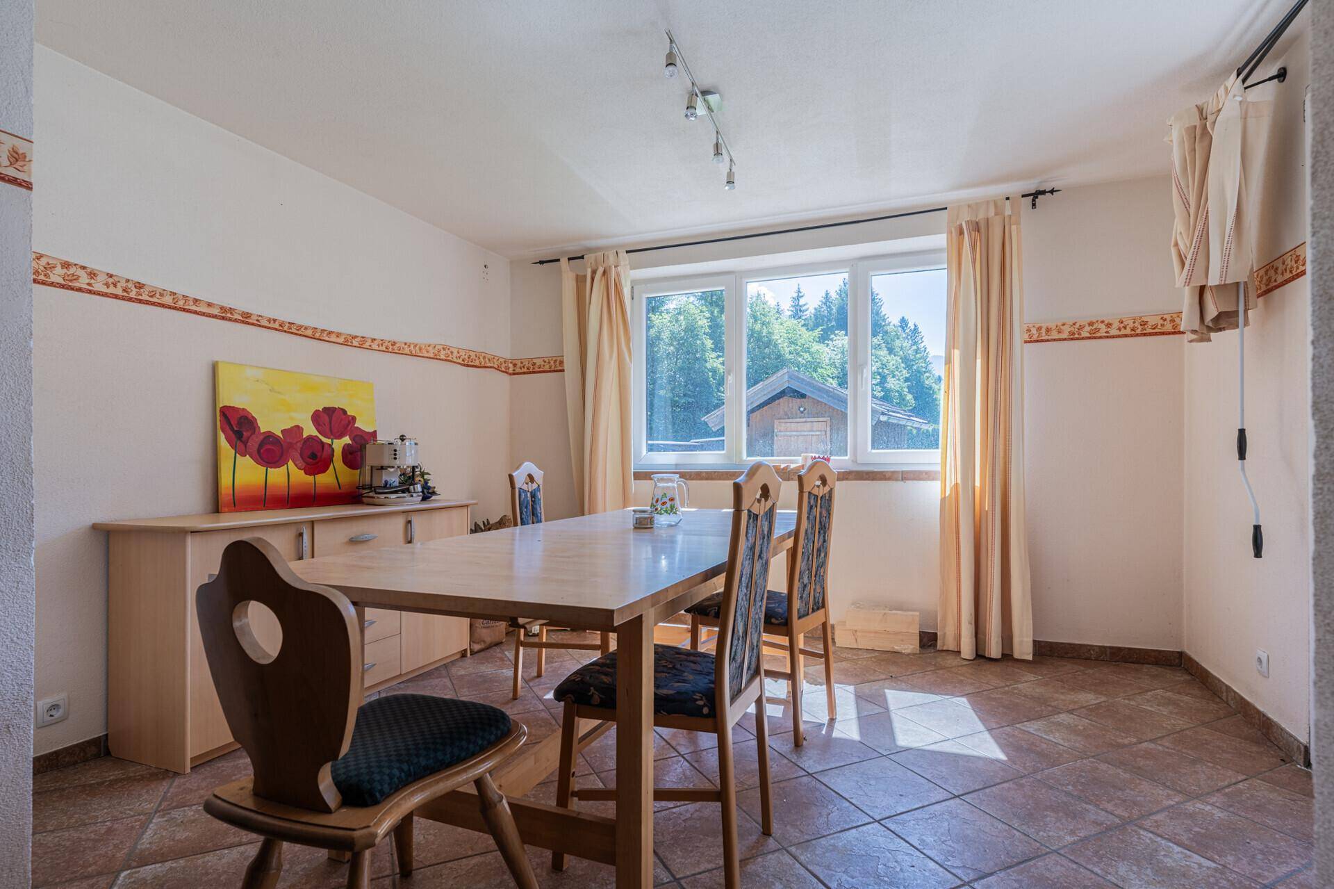 Gemütlicher Essbereich mit Holztisch, Fliesenboden und Fenster mit Blick ins Grüne.