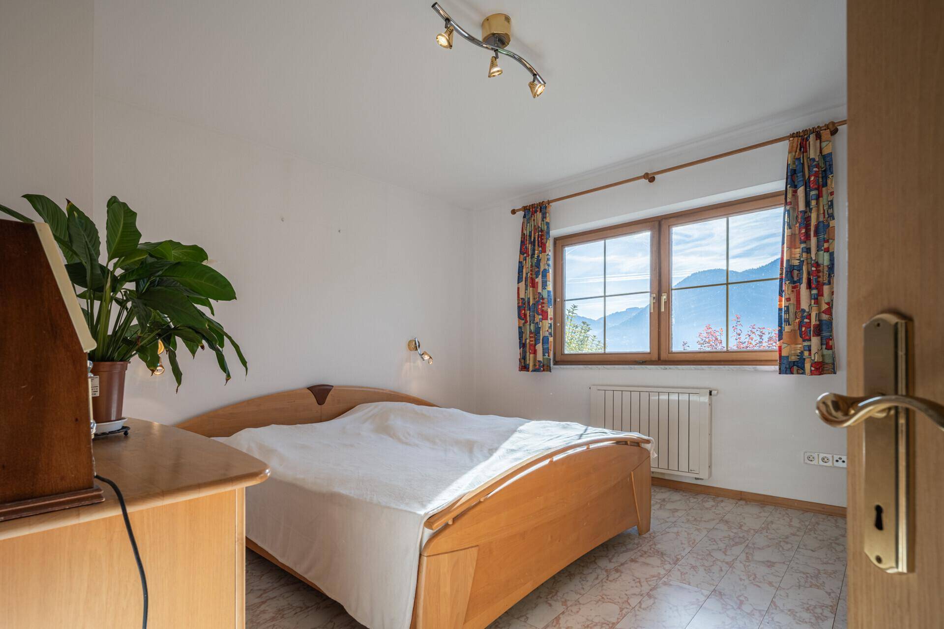 Helles Schlafzimmer mit Doppelbett, gemusterten Fliesen und Fensterblick auf die Berge.