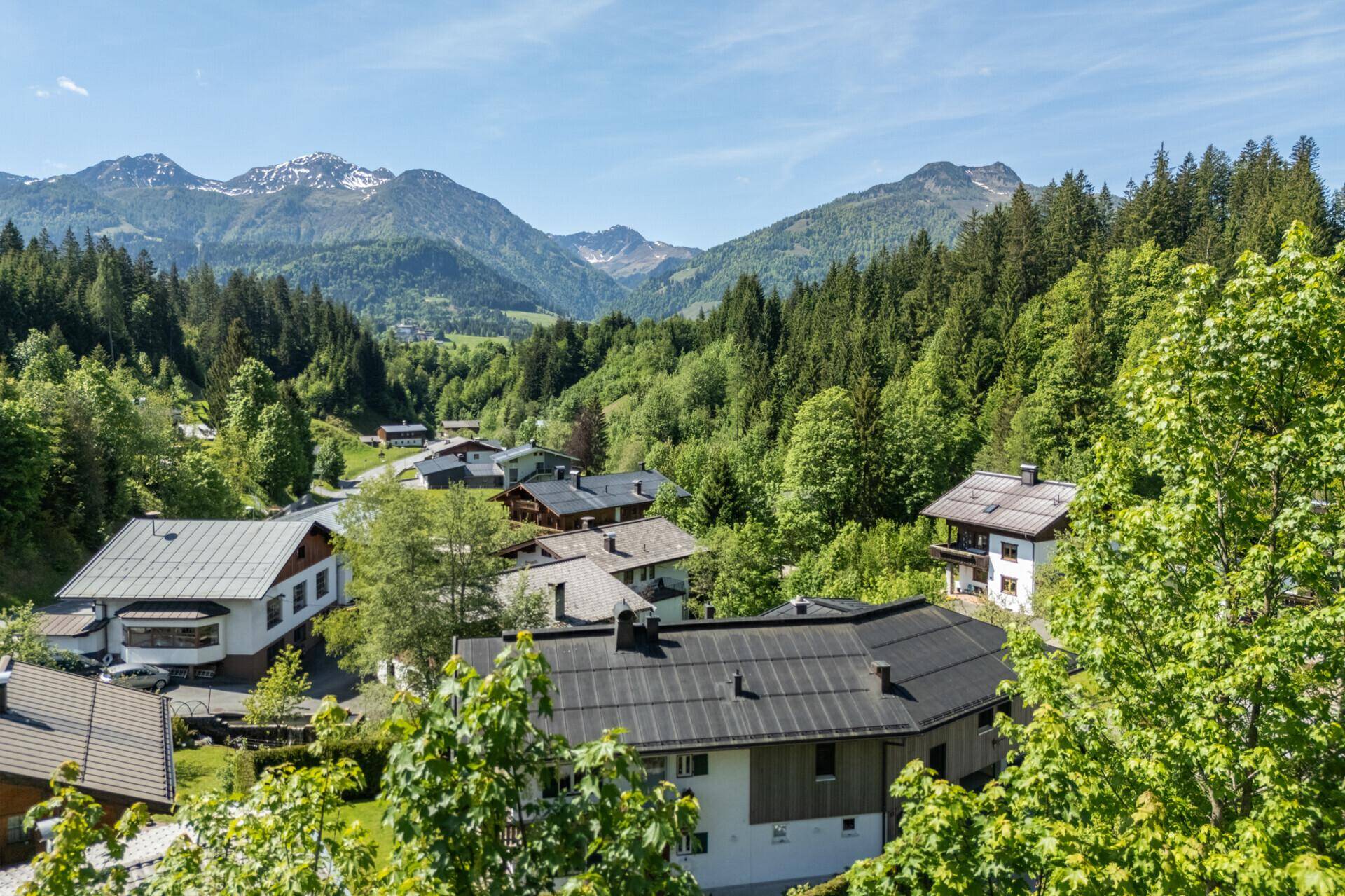 Panoramablick auf ein idyllisches Bergdorf, eingebettet in eine grüne Waldlandschaft mit majestätischen Gipfeln.