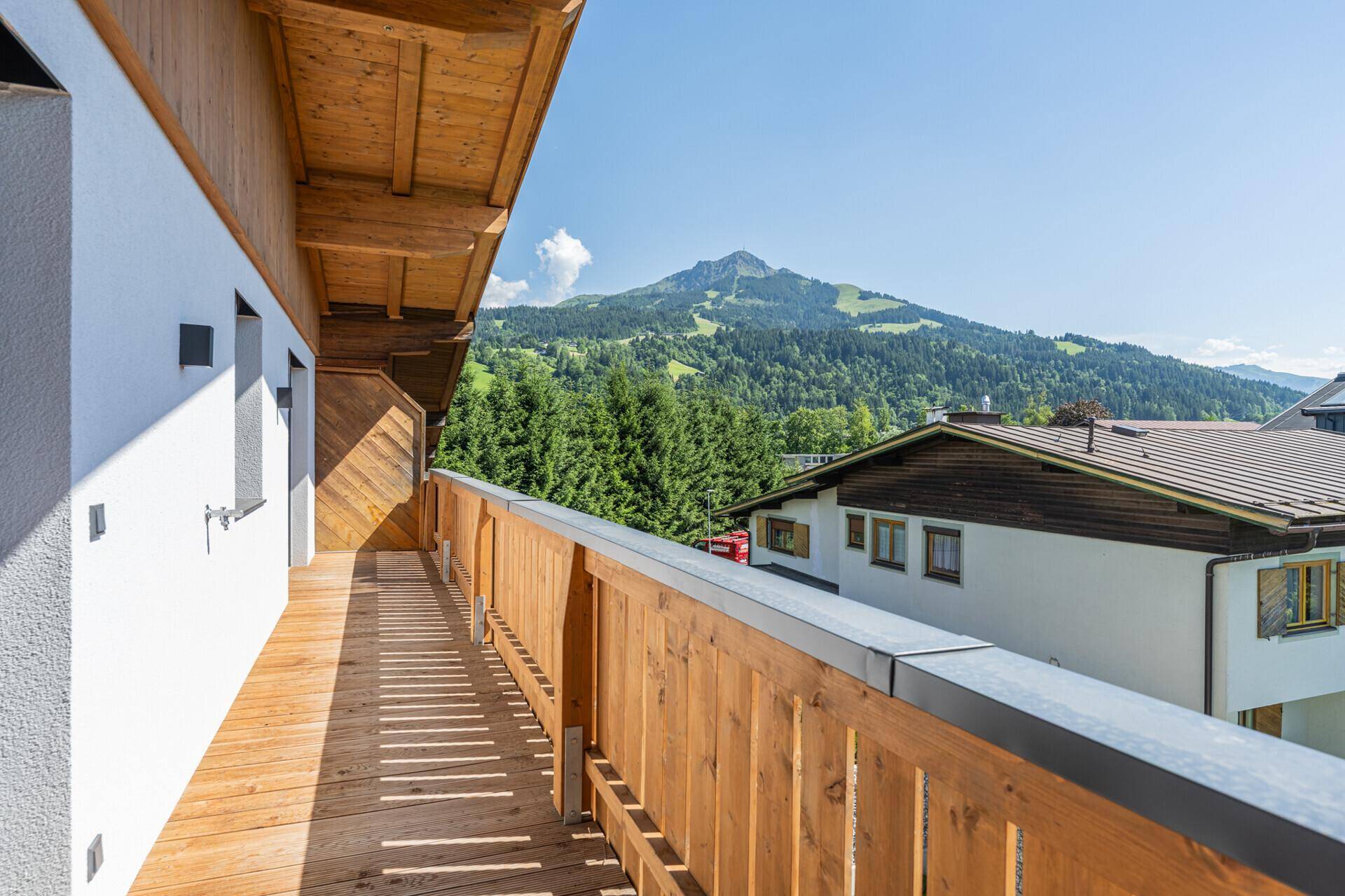 Langer Balkon mit Holzboden und Geländer, der einen weiten Blick auf die bewaldeten Berge bietet.