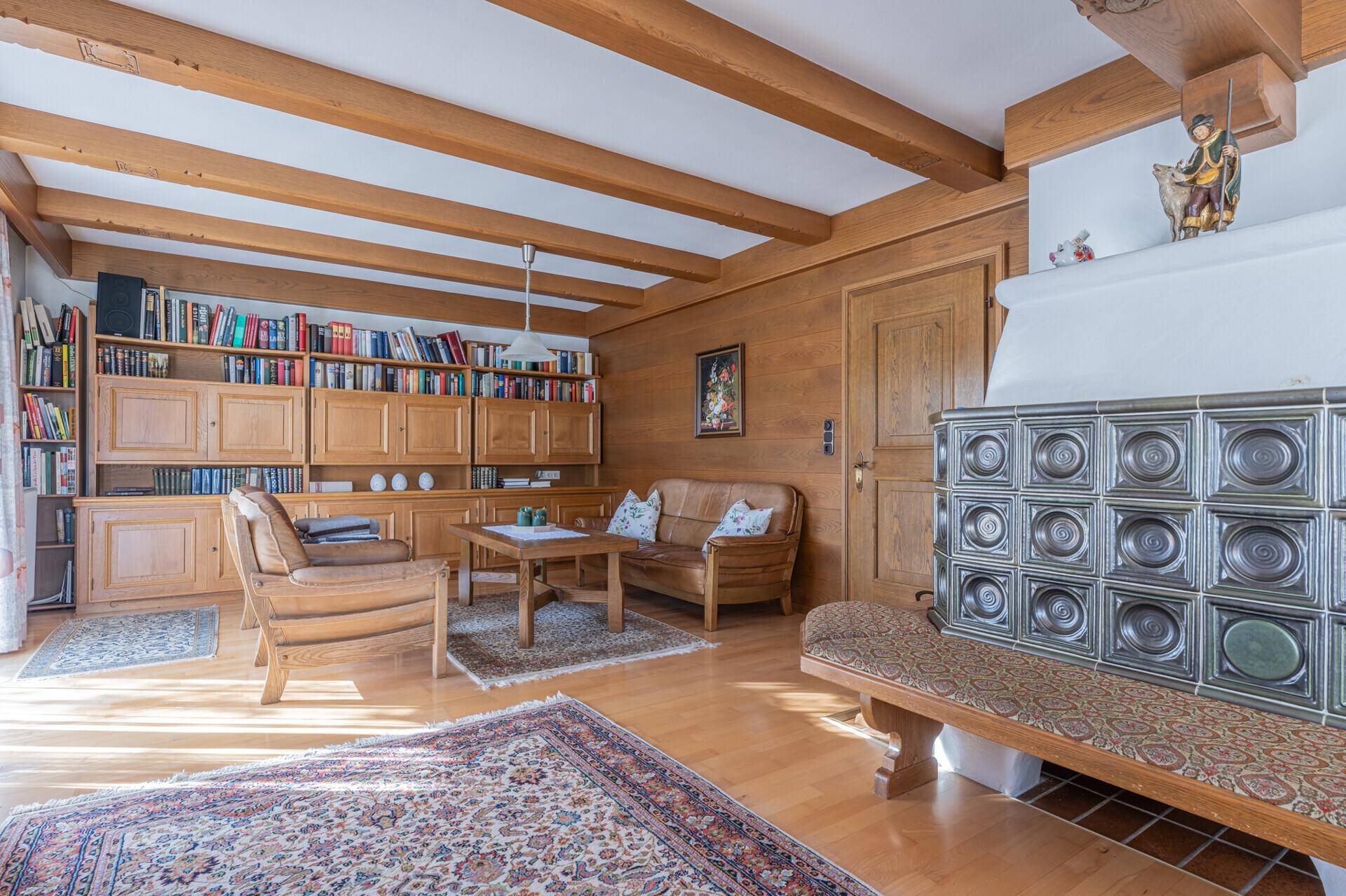 Gemütliches Wohnzimmer im alpenländischen Stil mit Holzbalken, Kachelofen und Bücherregalen.