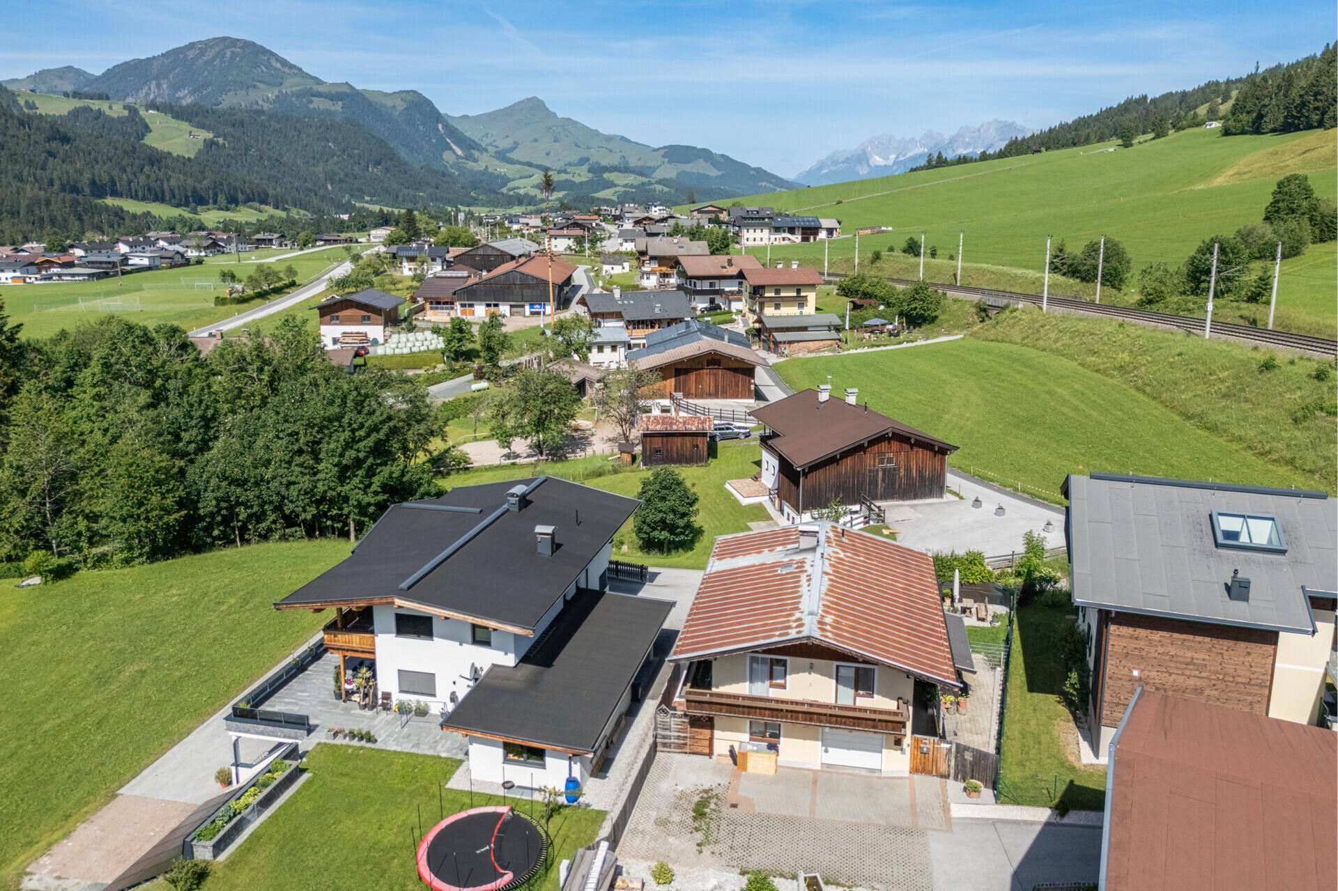 Luftaufnahme einer Wohnsiedlung in ländlicher Umgebung mit Bergen und grünen Wiesen.