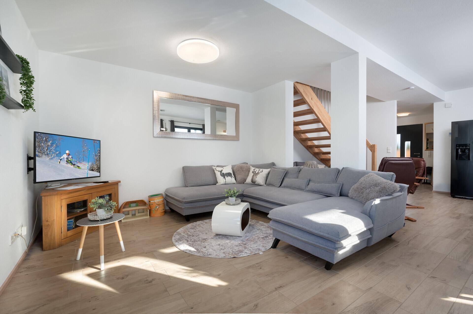 Gemütliches Wohnzimmer mit großem Ecksofa, Fernseher und Holzboden.