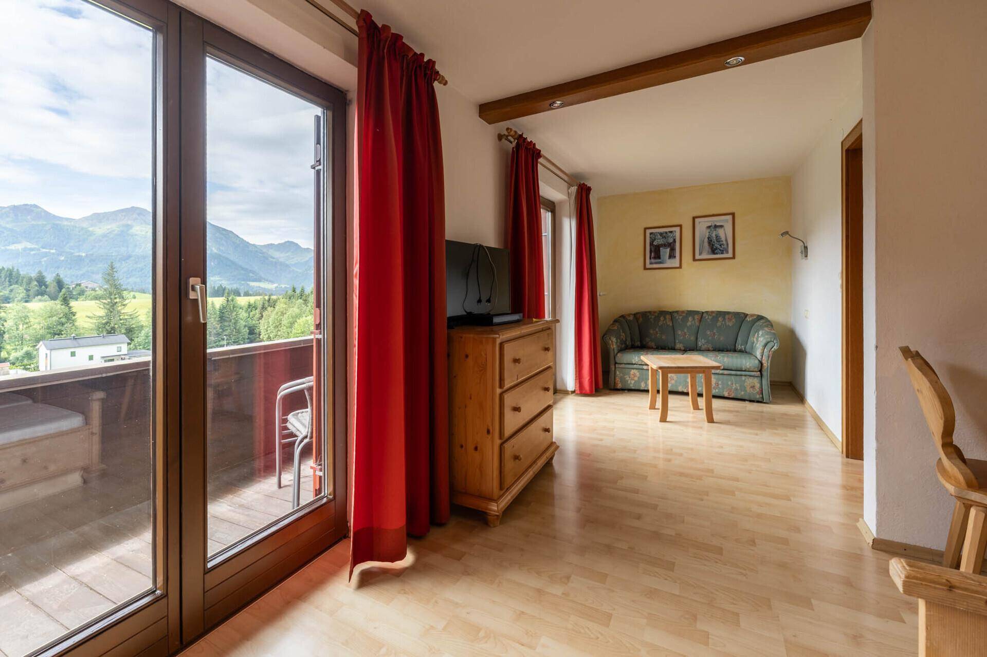 Heller Raum mit Holzboden, Sofa und Balkonzugang, der einen weiten Bergblick bietet.