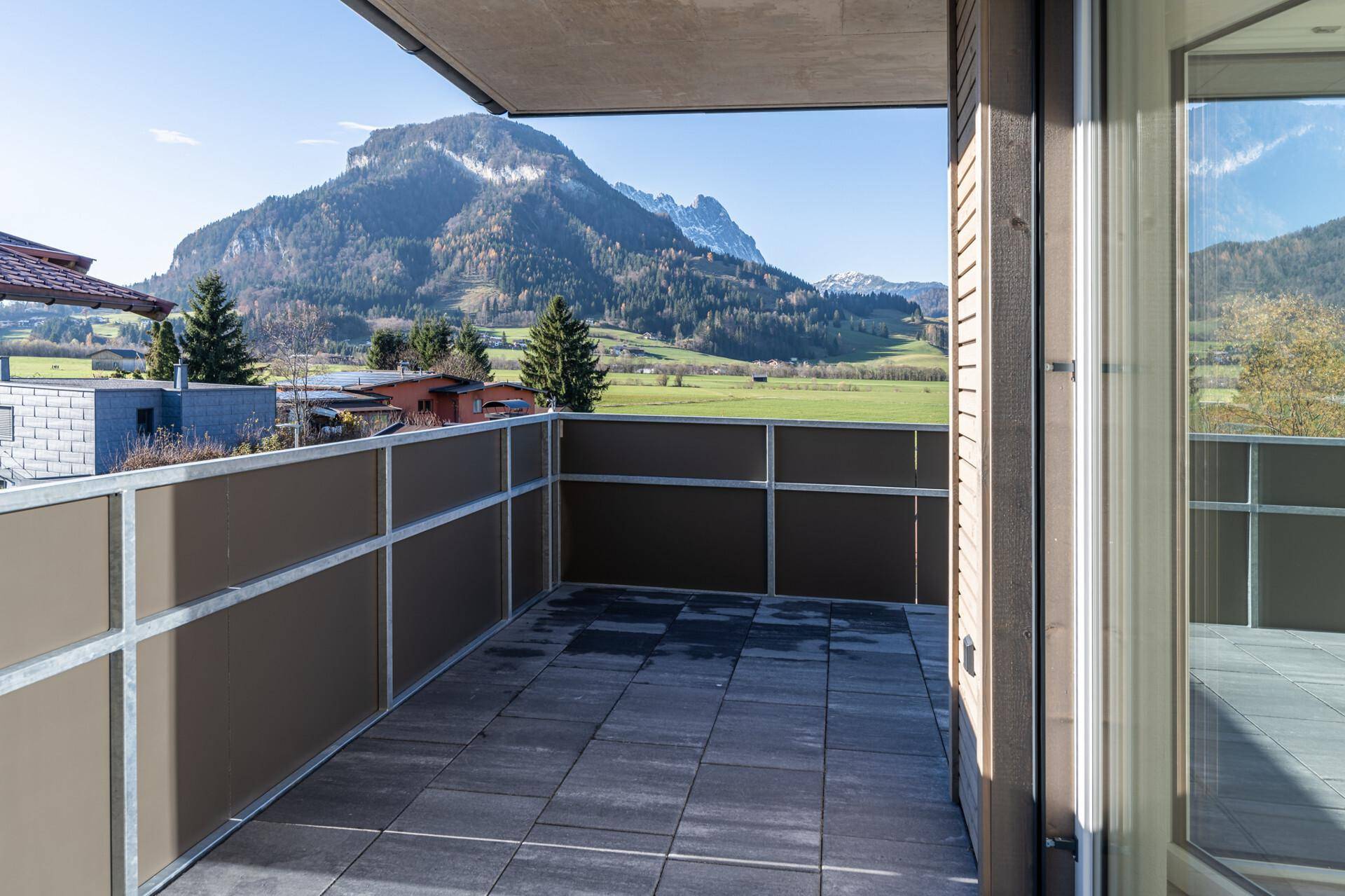 Kleiner Balkon mit Steinplattenboden und weitem Blick über grüne Felder und Berge.