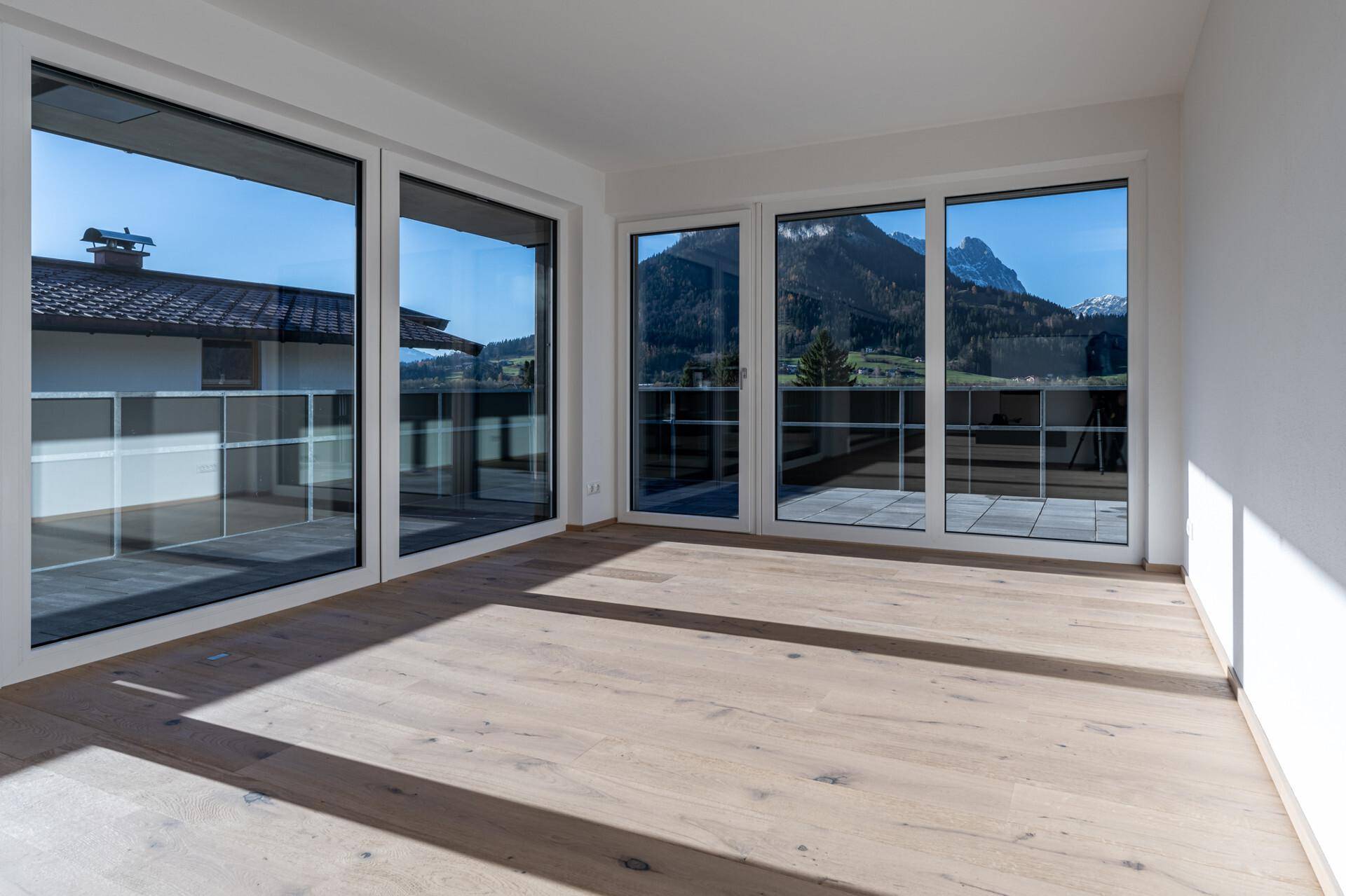 Wohnzimmer mit hellem Holzboden, großen Fenstern und beeindruckendem Bergblick.