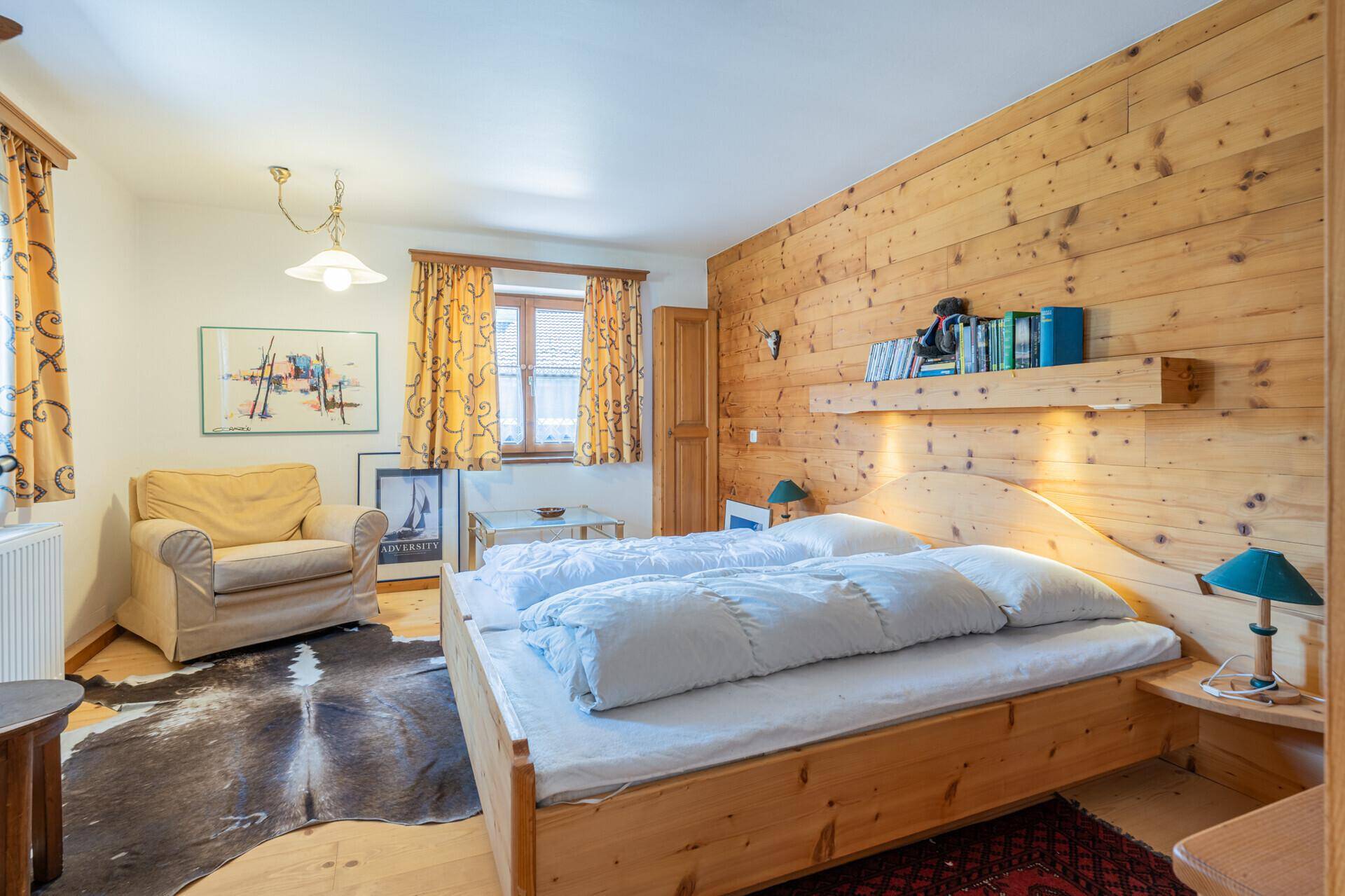 Gemütliches Schlafzimmer mit Holzwandverkleidung, Doppelbett und einem Sessel.
