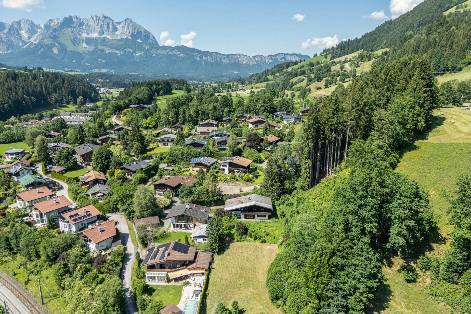 Sonnige Luftaufnahme einer Wohngegend in den Alpen mit vielen Häusern und üppiger Vegetation.