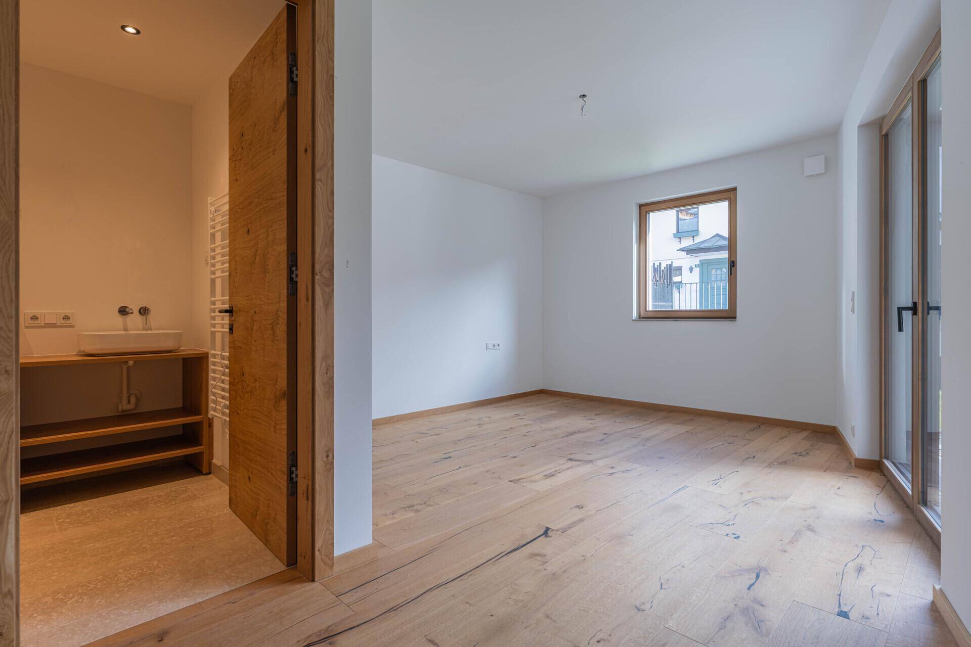 Helles Zimmer mit Holzboden und Zugang zu einem modernen Badezimmer.