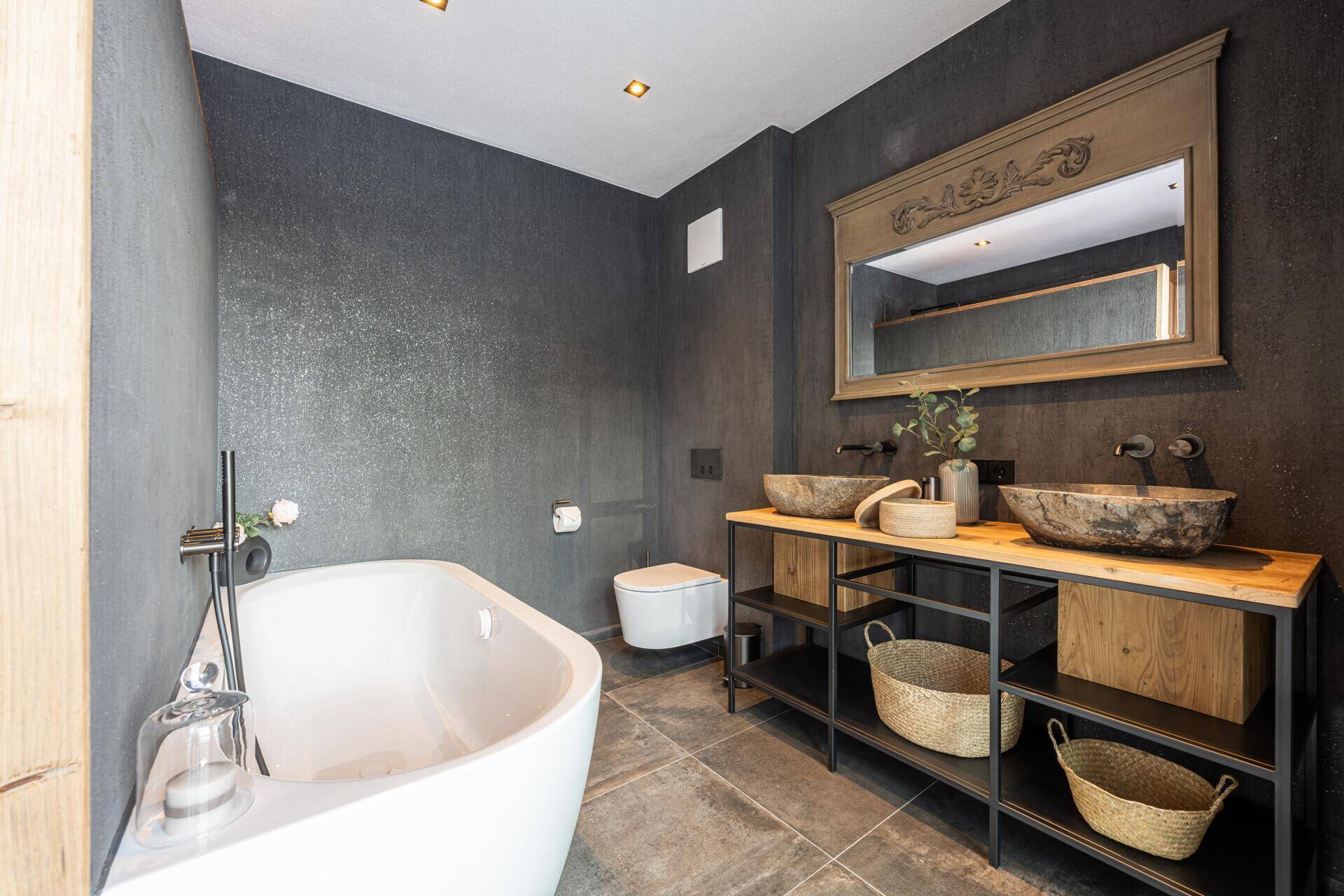 Modernes Badezimmer mit freistehender Badewanne, Doppelwaschbecken und dunklen Wänden.