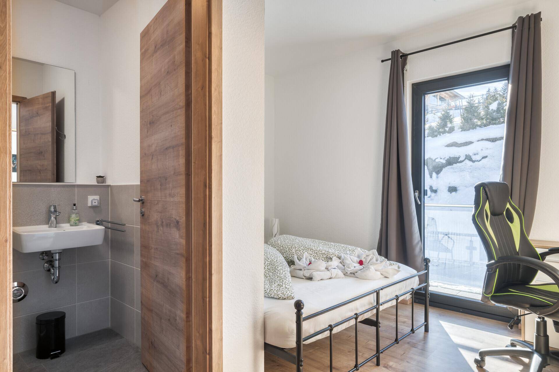 Schlafzimmer mit Bett und angrenzendem kleinen Badezimmer mit Waschbecken.