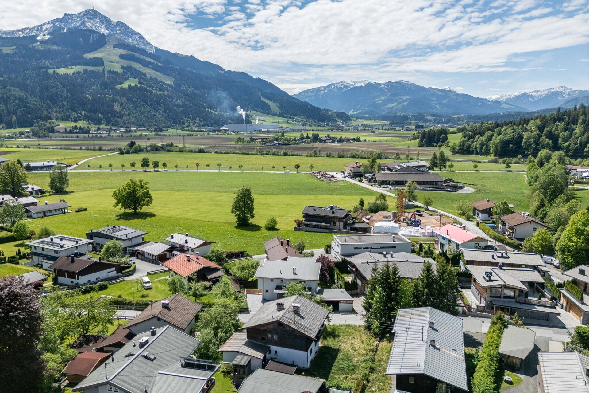 Weitläufiger Blick über ein Tal mit Siedlung, grünen Feldern und schneebedeckten Bergen im Hintergrund.