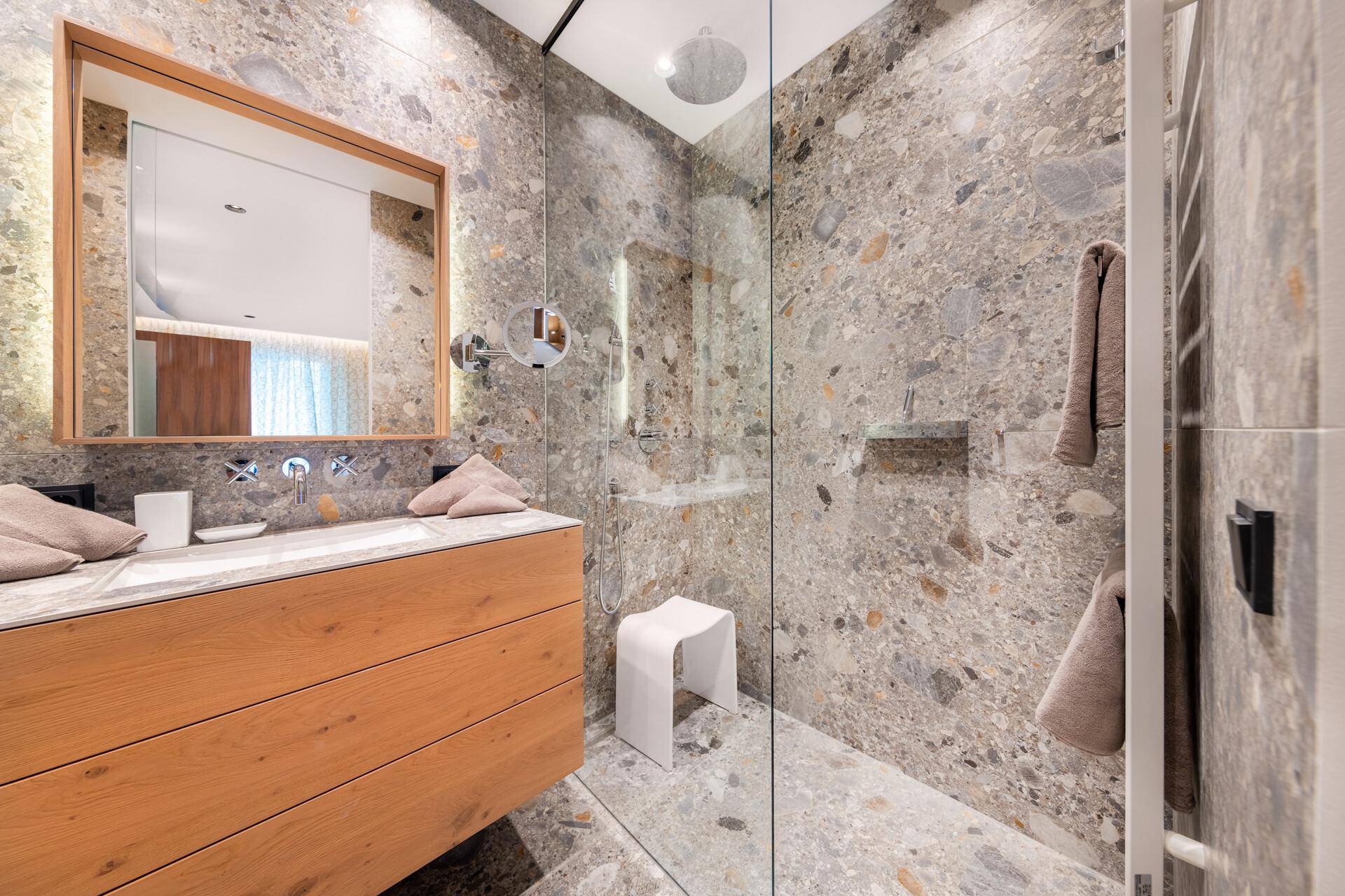 Elegantes Badezimmer mit begehbarer Dusche, Steinfliesen und modernem Holzwaschtisch.