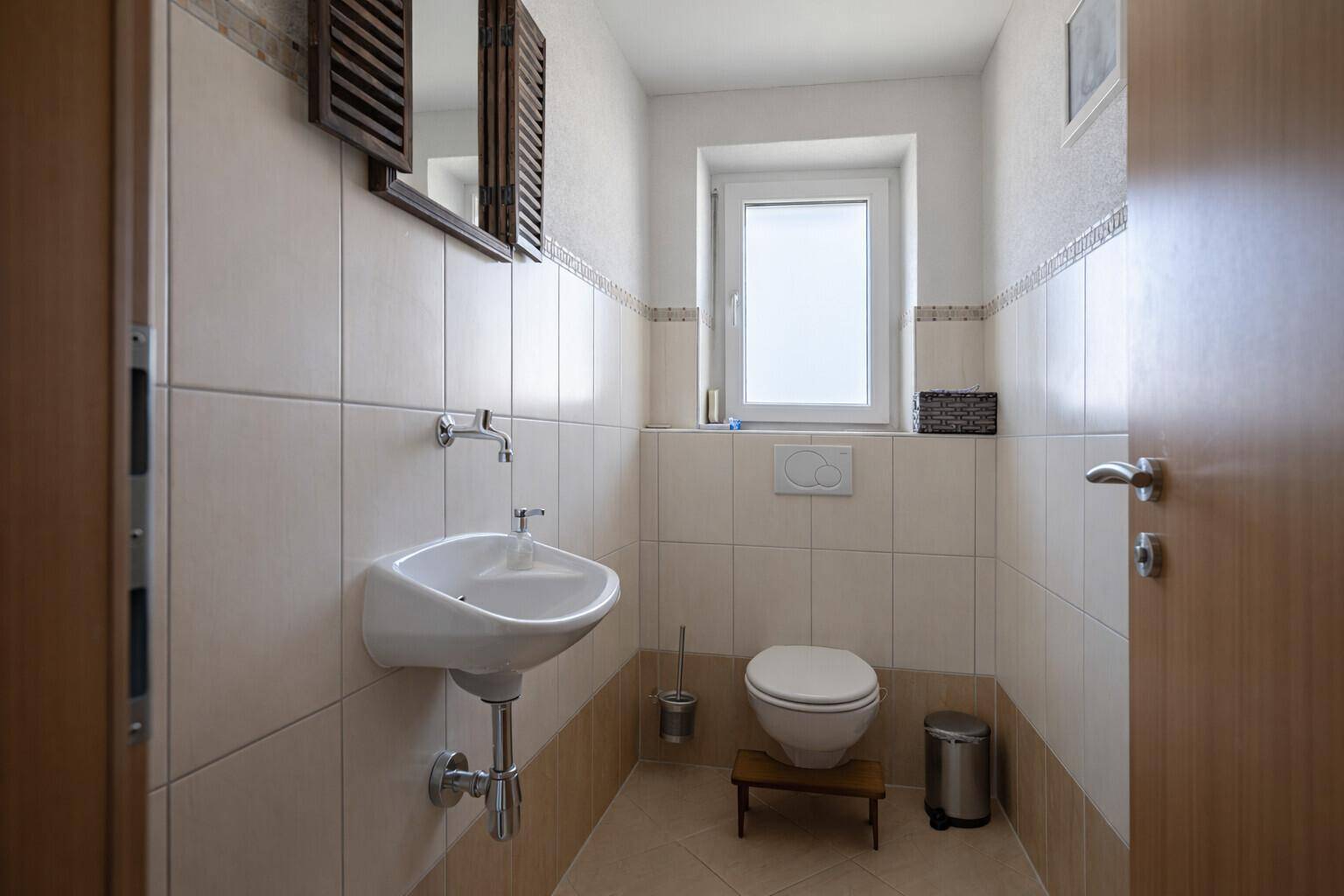Kleines Gäste-WC mit Fenster, Wandwaschbecken und hellen Fliesen.