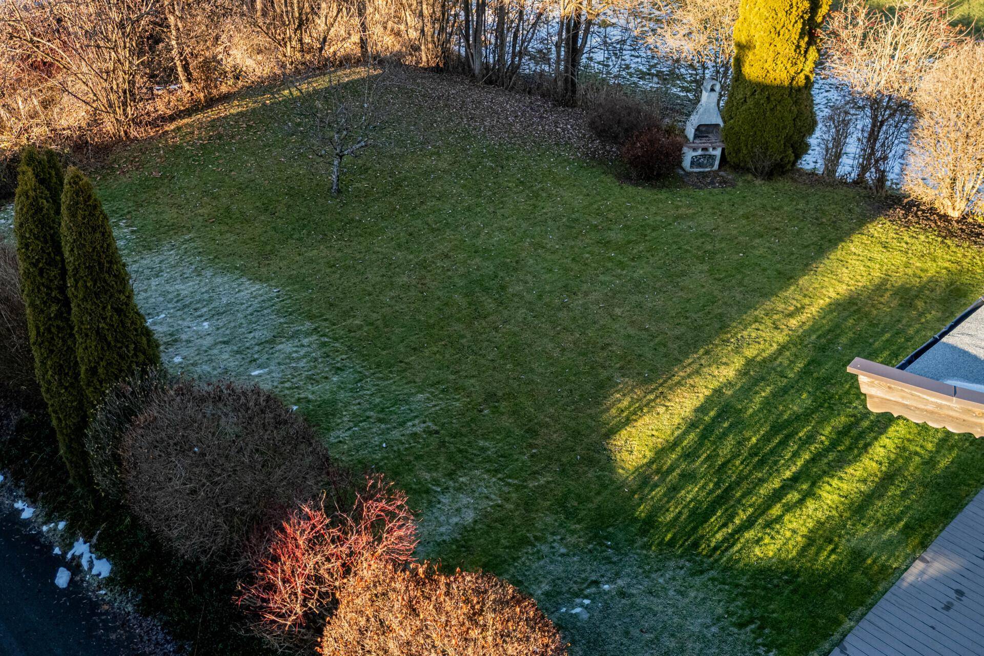 Luftaufnahme des weitläufigen Gartens mit Rasenfläche, Bäumen und einem gemauerten Grillplatz.